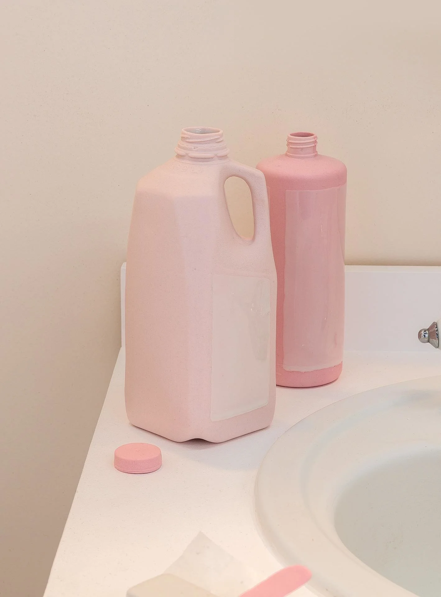 Detail shot of a pink porcelain milk jug, shampoo bottle, and bottle cap on the counter.