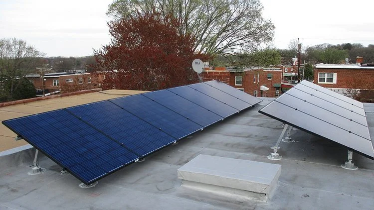 Solar panels installed on a flat rooftop with trees and buildings in the background.