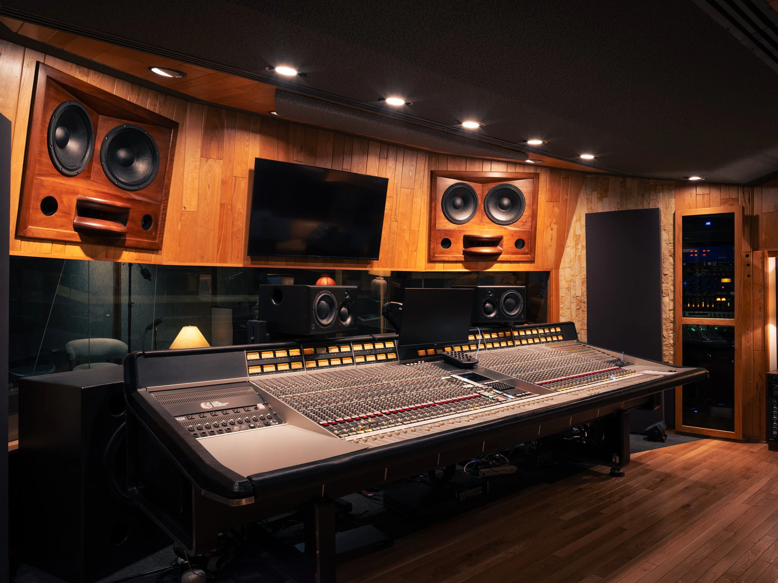 Recording studio with wooden walls, large speaker monitors, a mixing console, and audio equipment.