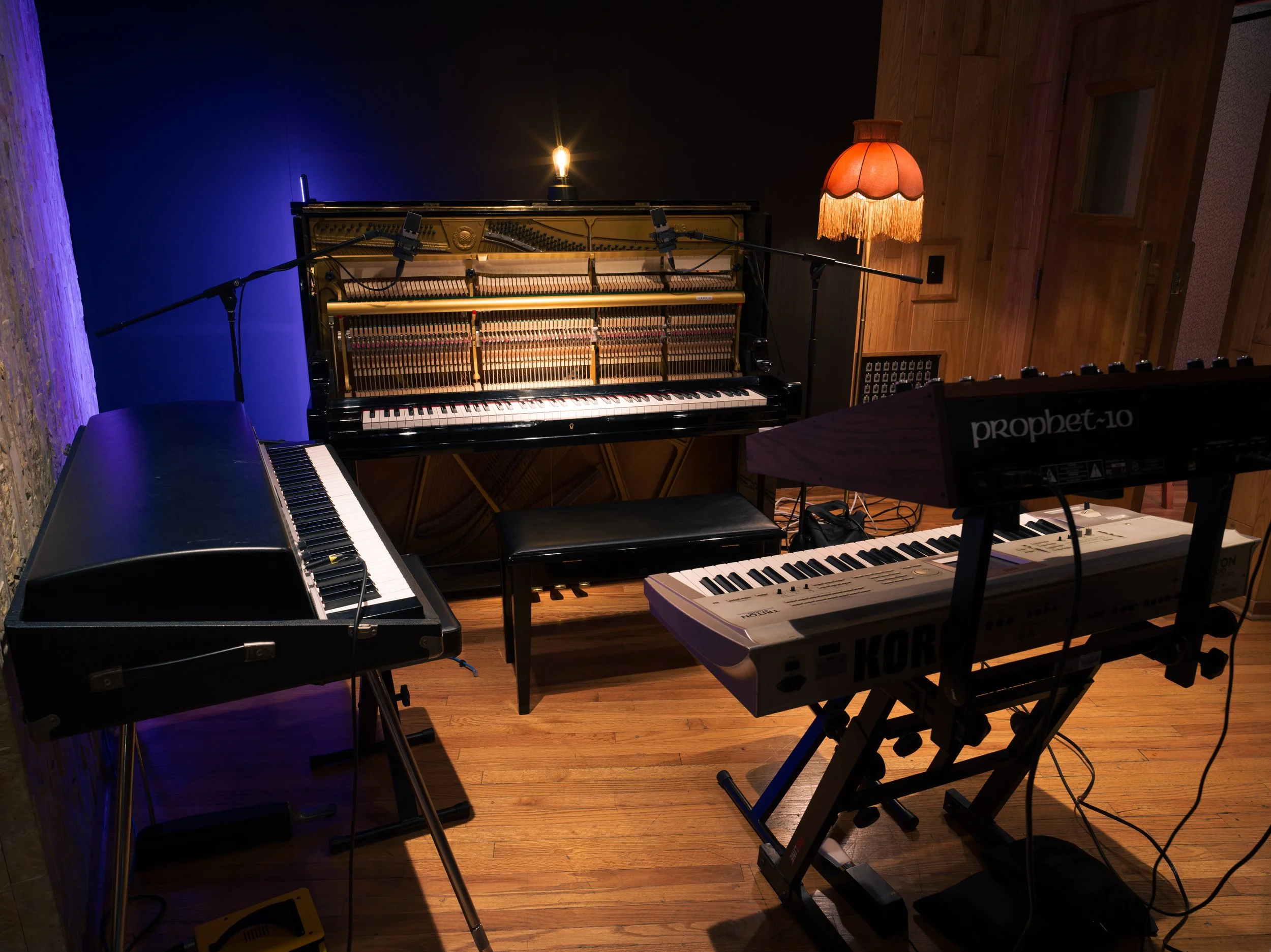 A music recording studio with a piano, a keyboard, and a digital keyboard surrounded by microphone stands and cables.
