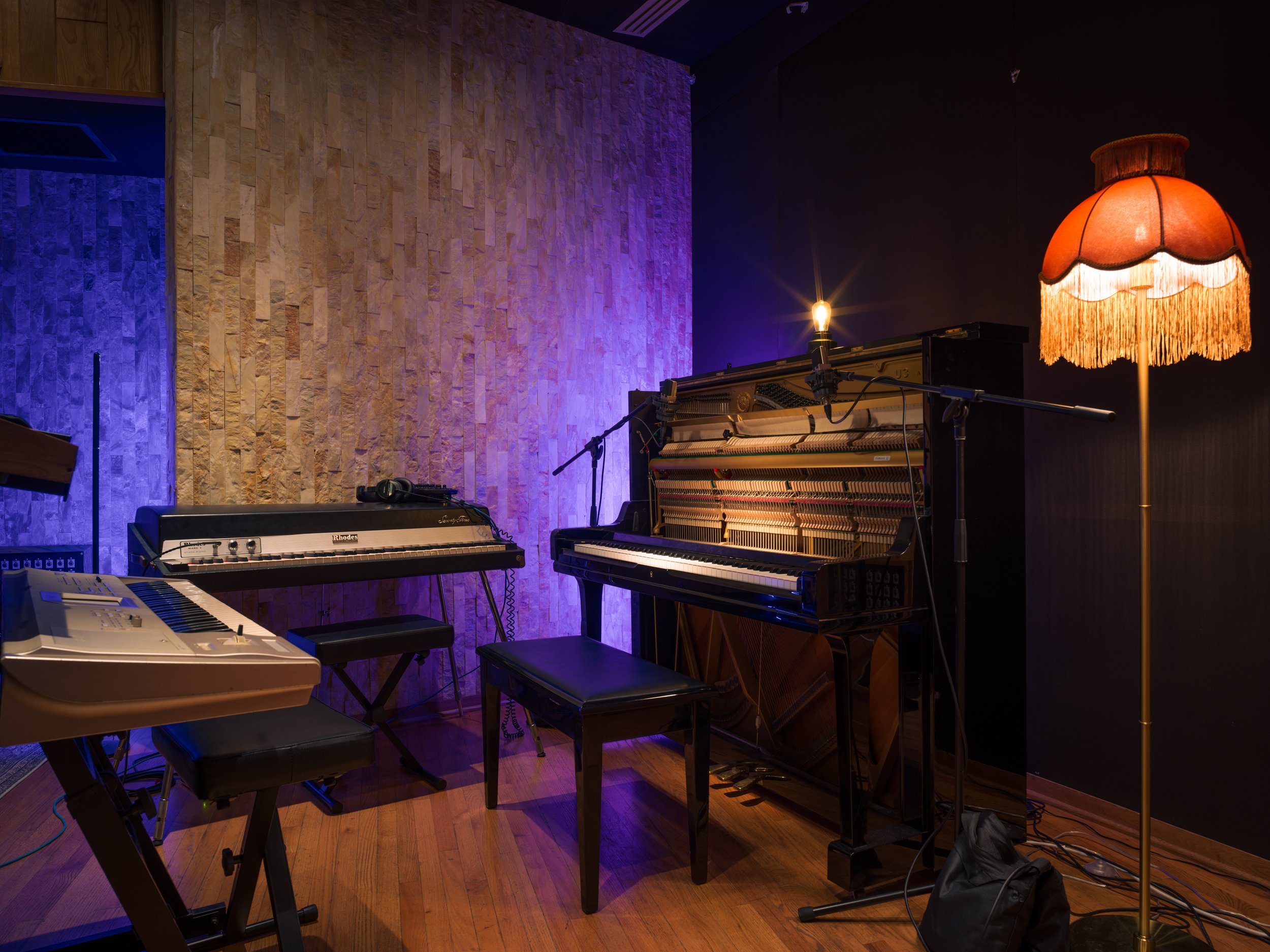 Music room with upright piano, digital keyboard, and vintage lamp with orange fringed shade.