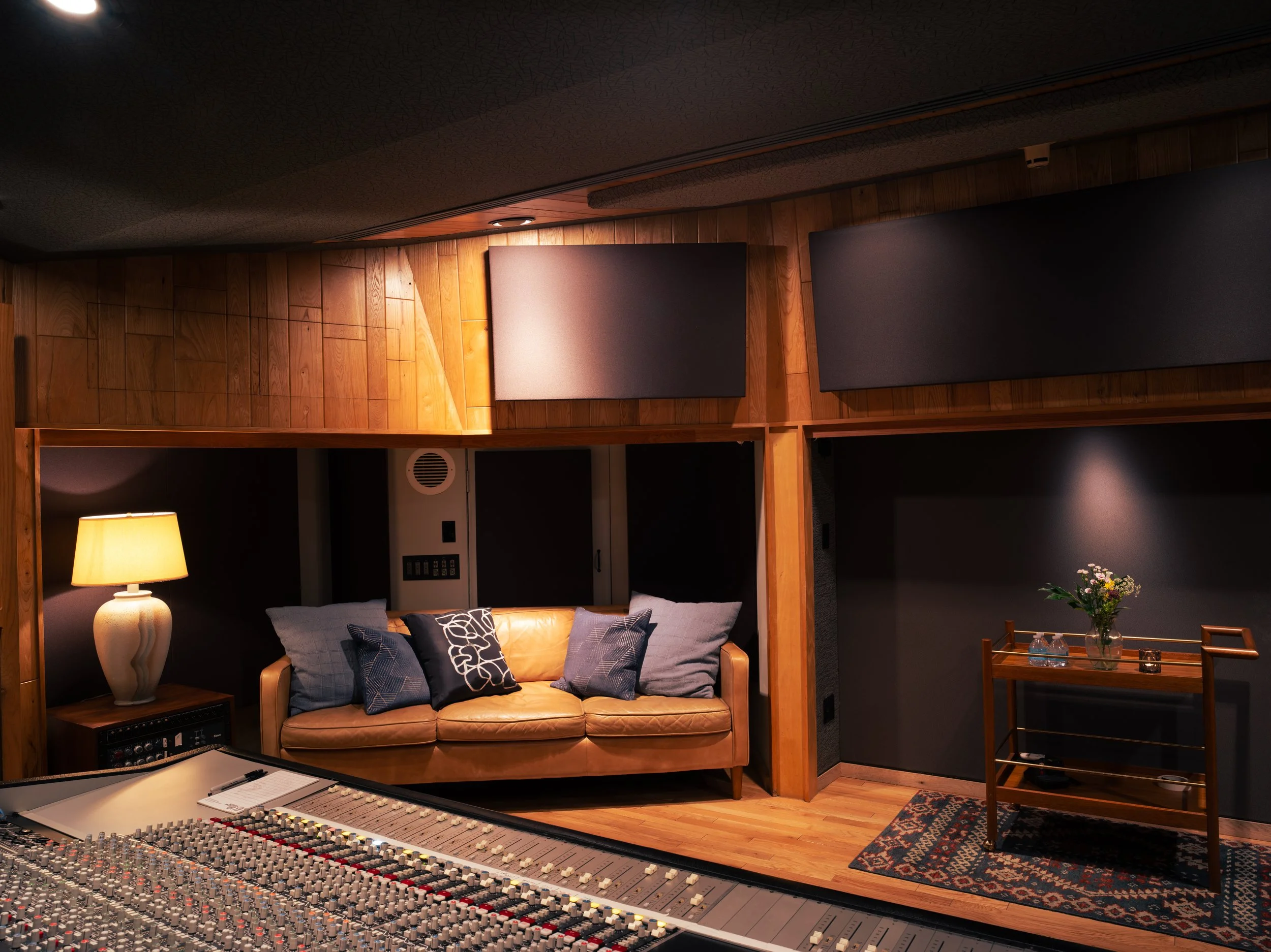 Recording studio with a leather sofa, a table with a flower arrangement, and a sound mixing console.