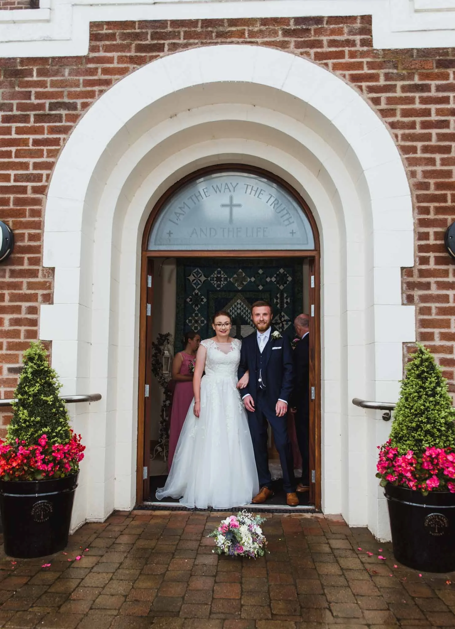 New husband and wife at the entrance of the church for a portrait with bouquet on the ground.