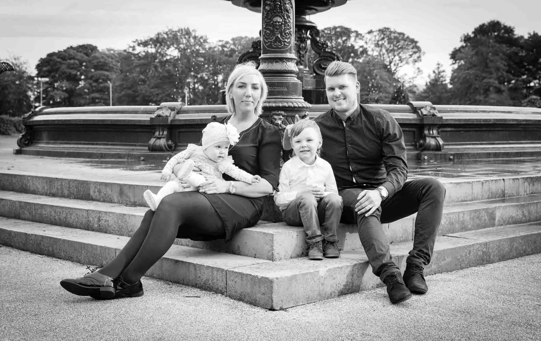 Mono image of the family sitting at the fountain, smiling at the camera.