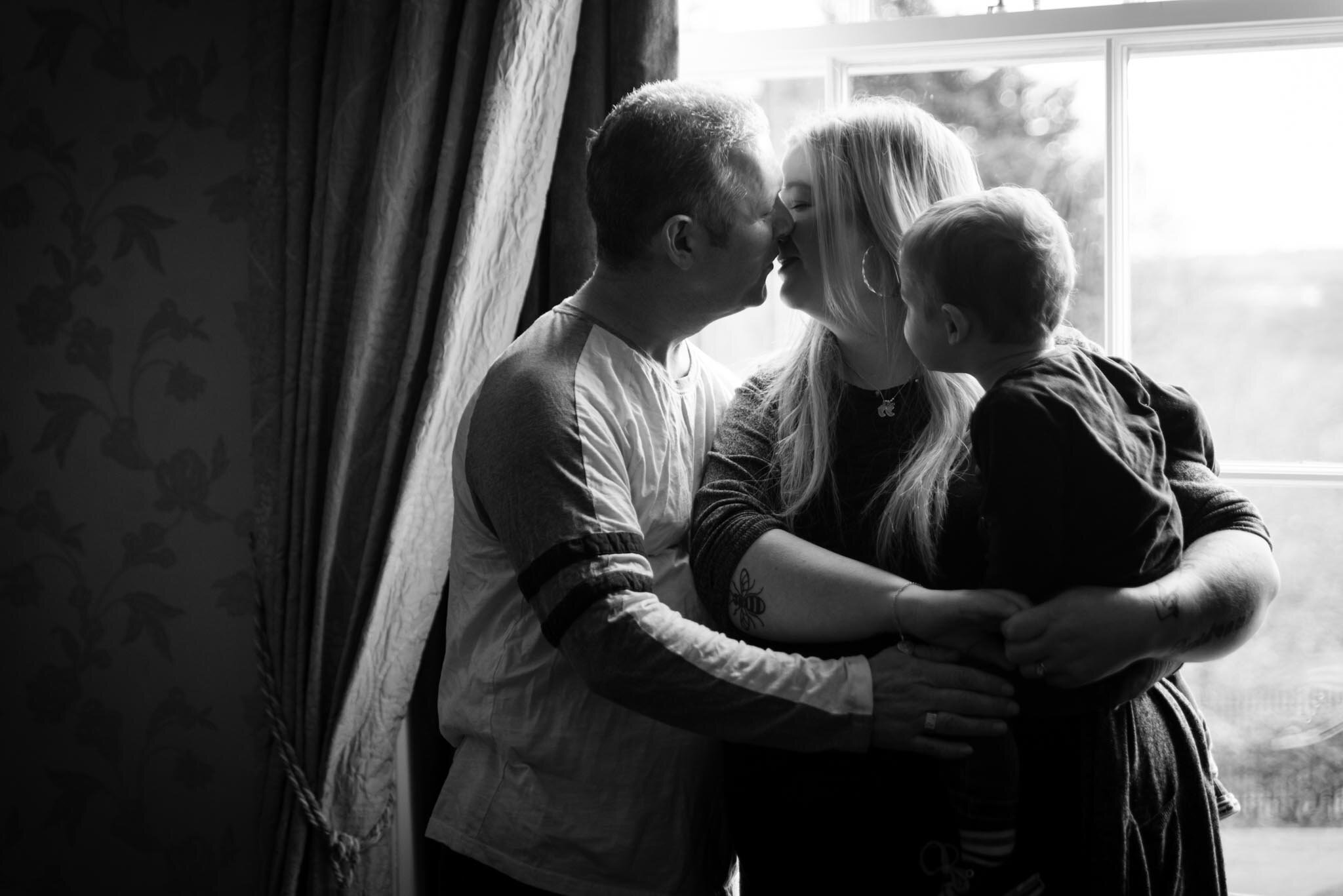  Black and white kissing in front of window with son watching 