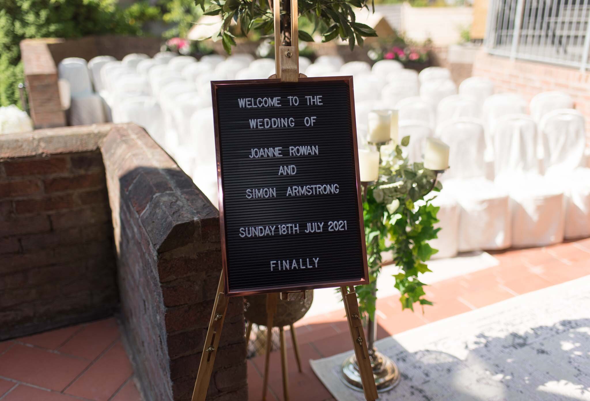  Signage displaying the date of the wedding on a board sitting on an easel at the back of The Rabbit ready for the ceremony with empty chairs behind. 