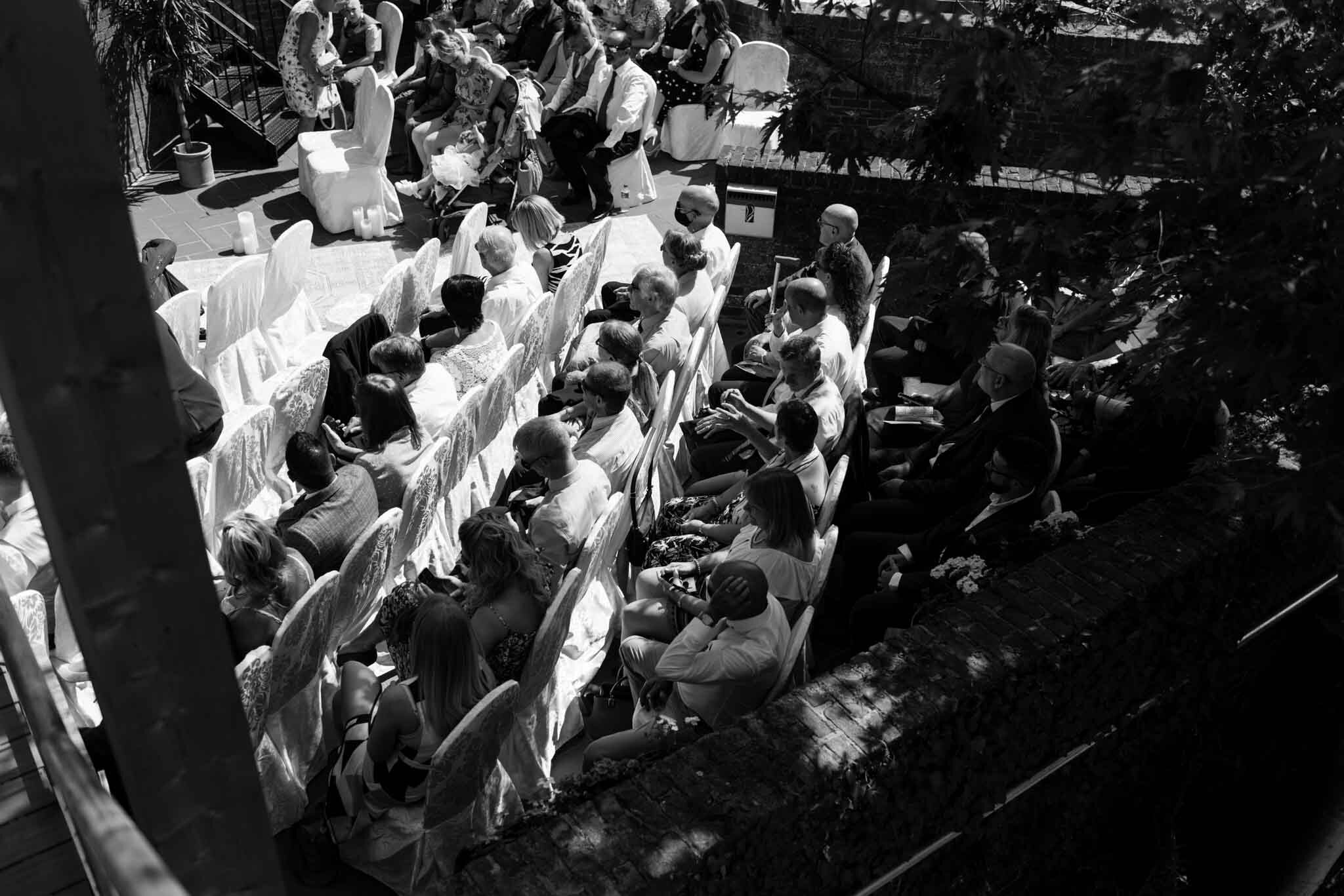  Moody black and white image looking down on the guests showing light and dark watching the ceremony. 