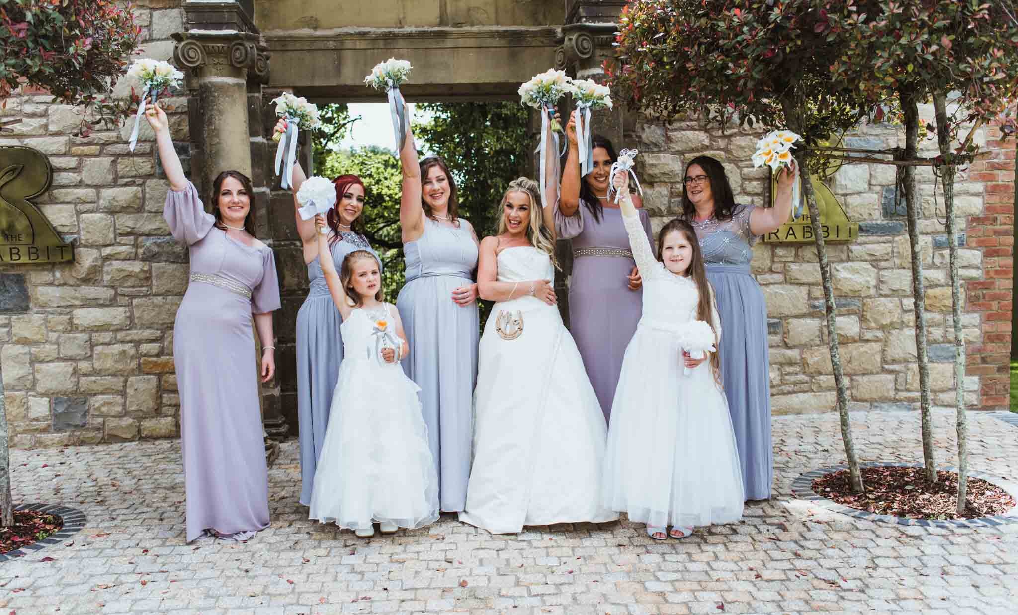  Bride and bridesmaids cheering at the back of the venue with bouquets up in the air. 