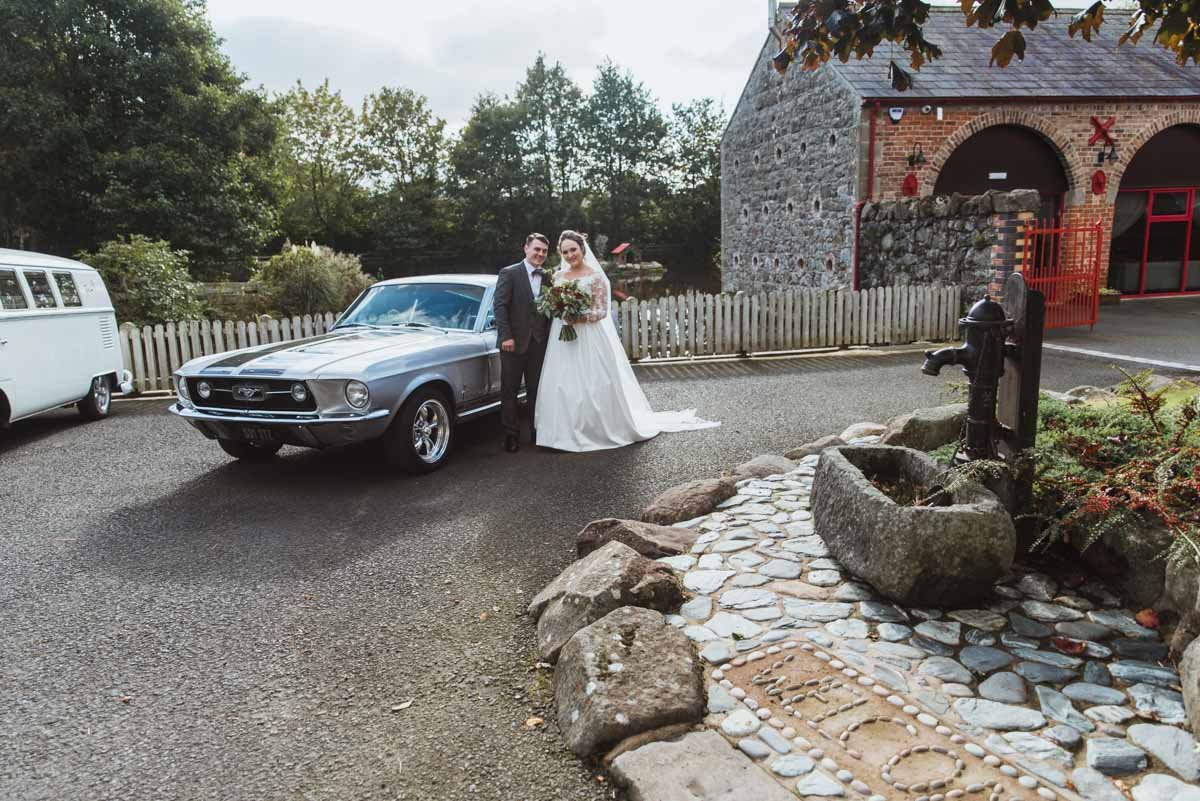  One of the best wedding venues in Craigavon with the couple in the front area beside the water pump standing beside the car. 