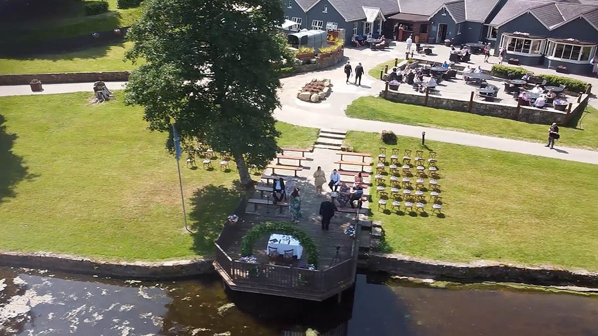  Outside as the ceremony gets ready with drone from the sky looks down beside the water. 