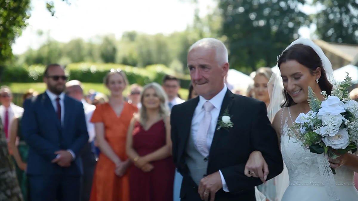  Father walking daughter holding bouquet down aisle as guests are watching outside. 