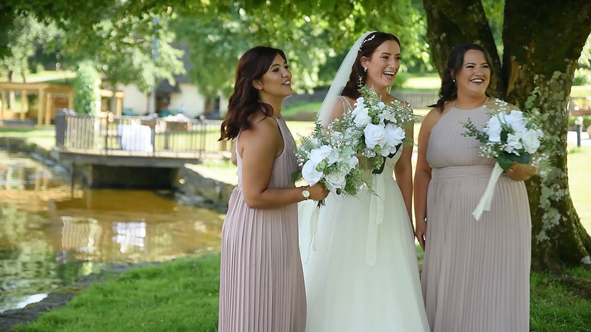  Bride with bridesmaids beside a tree with bouquets and a boat in the water to the left. 