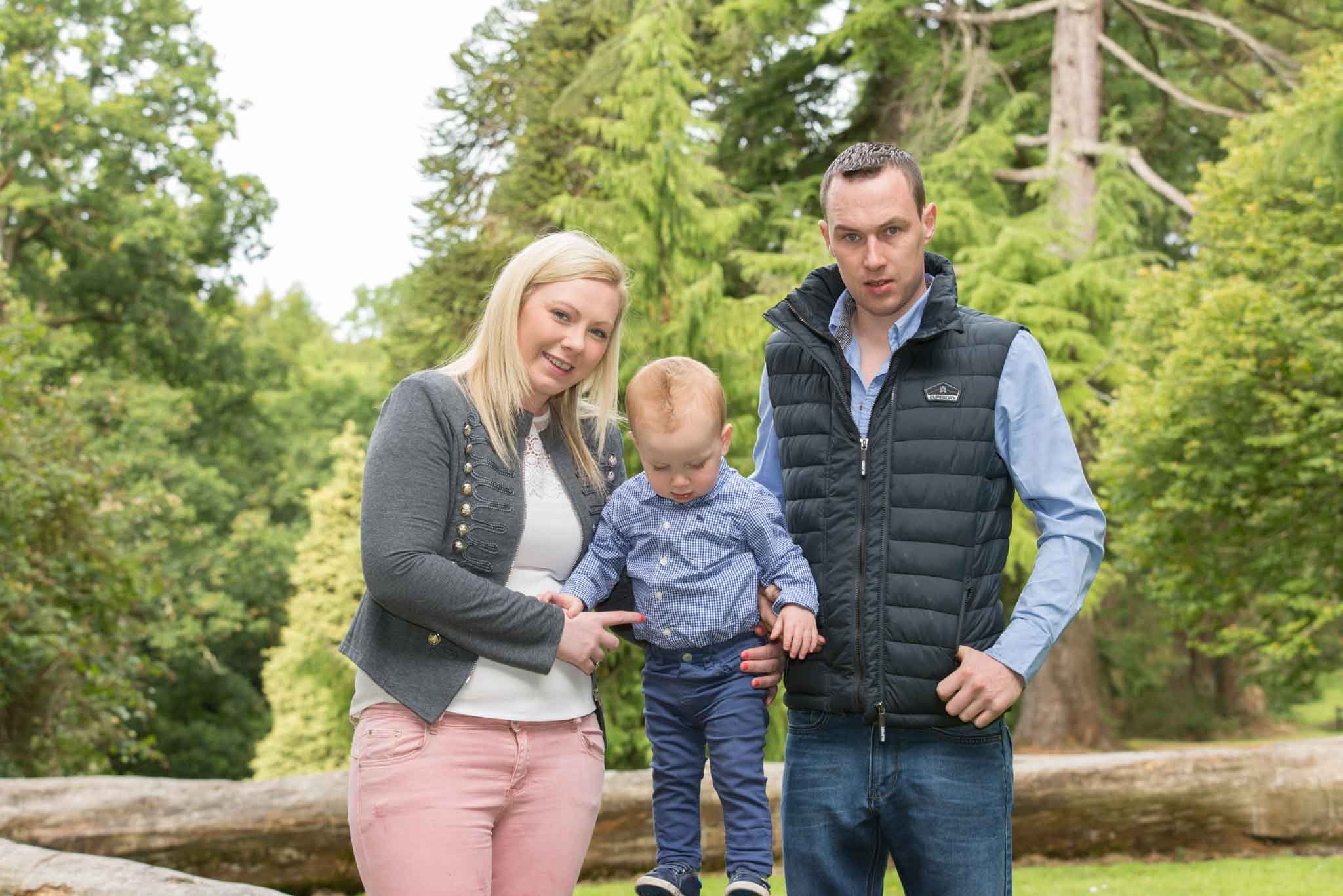 Two adults with a child looking down with plenty of trees and sky in the background.