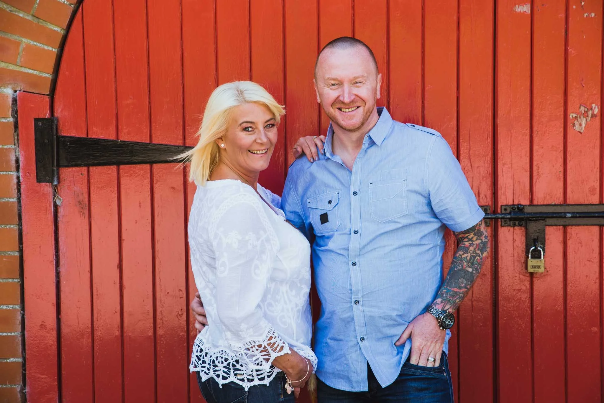  The couple is in front of the large red barn doors. 