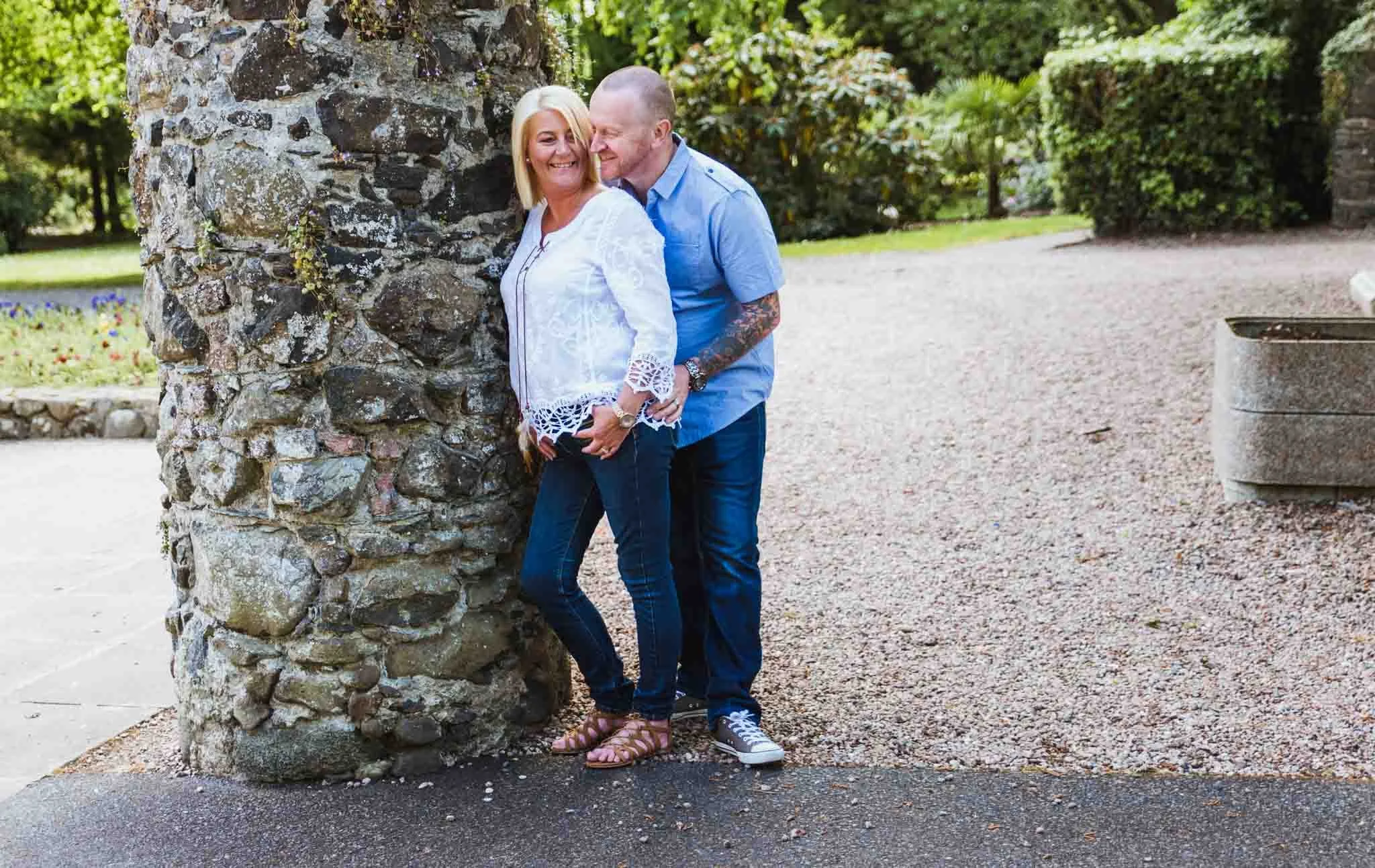  An engaged couple standing beside a stone pillar holding each other. 