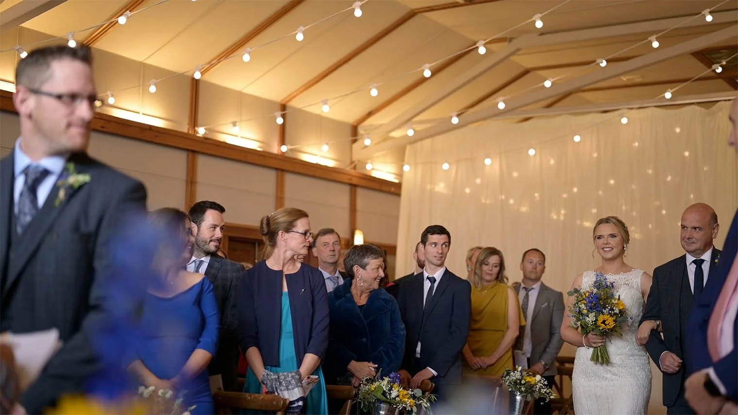 The bride, with father walking down the aisle, as the groom turns around to look during the ceremony.
