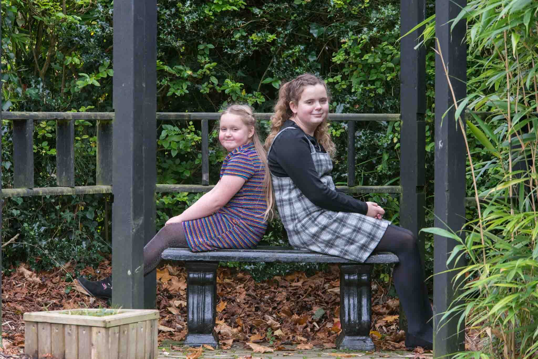 Two young sisters sitting back to back.