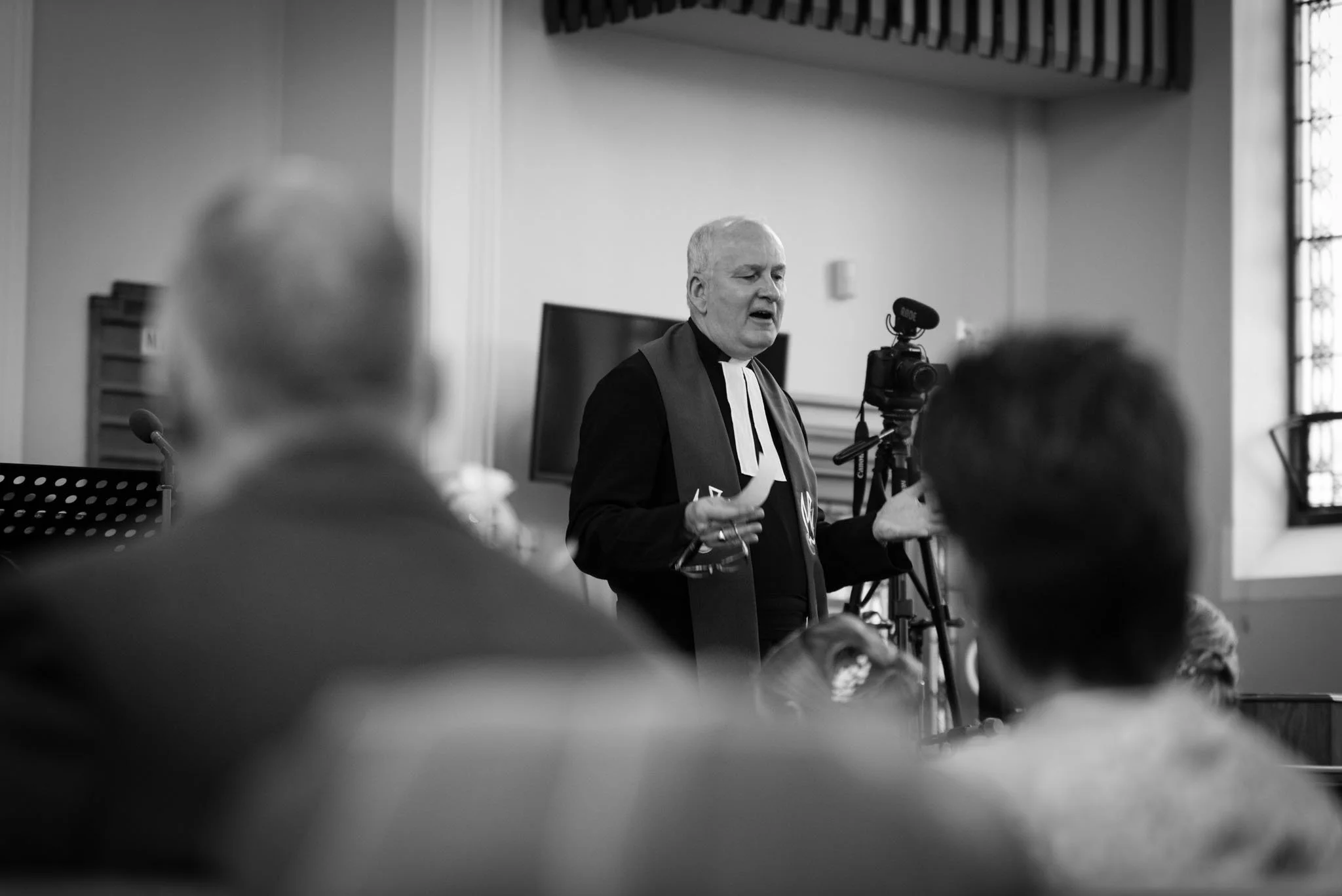 Mono image of the minister with backs of people blurred out.