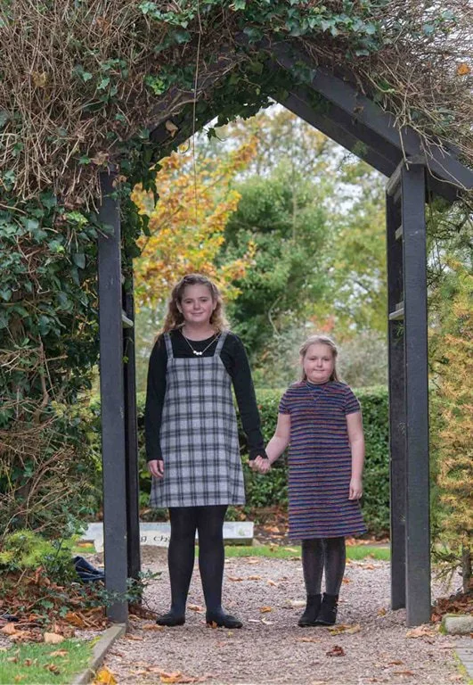 Sisters holding hands under a wooden archway.