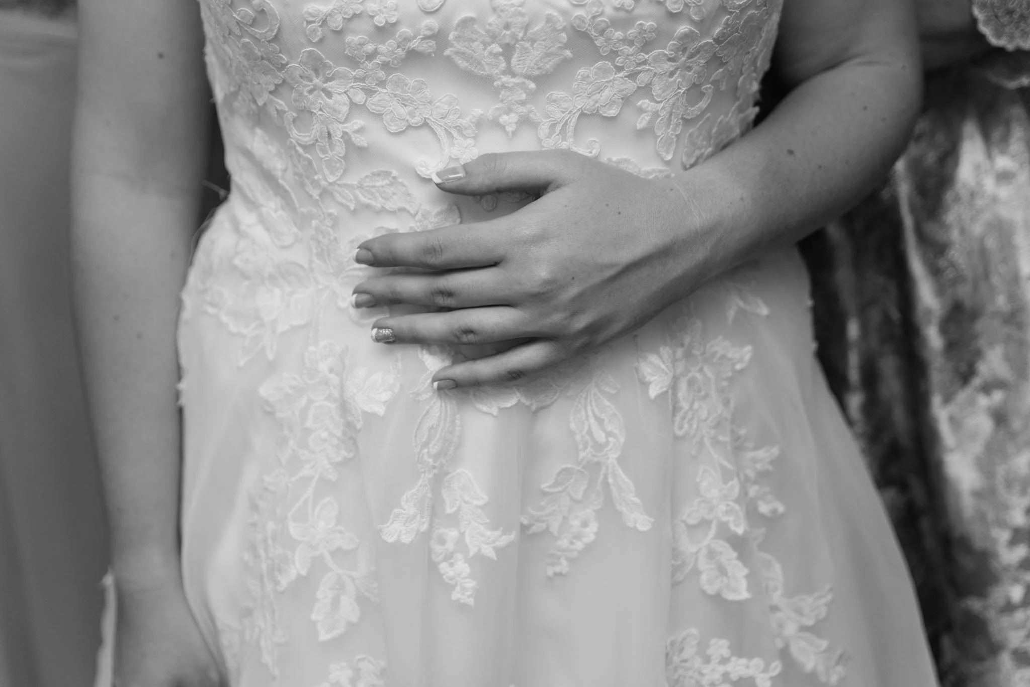 Mono photo of the bride's hand on her stomach with the dress on.