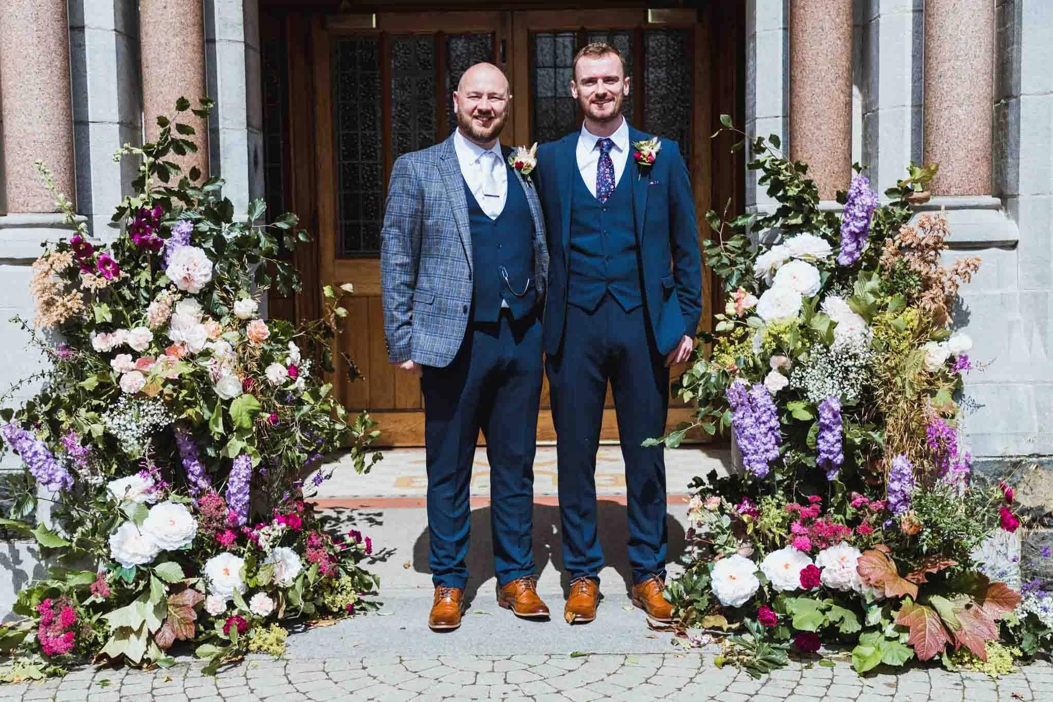 Groom with bestman at the front of the church with lots of flowers on both sides.