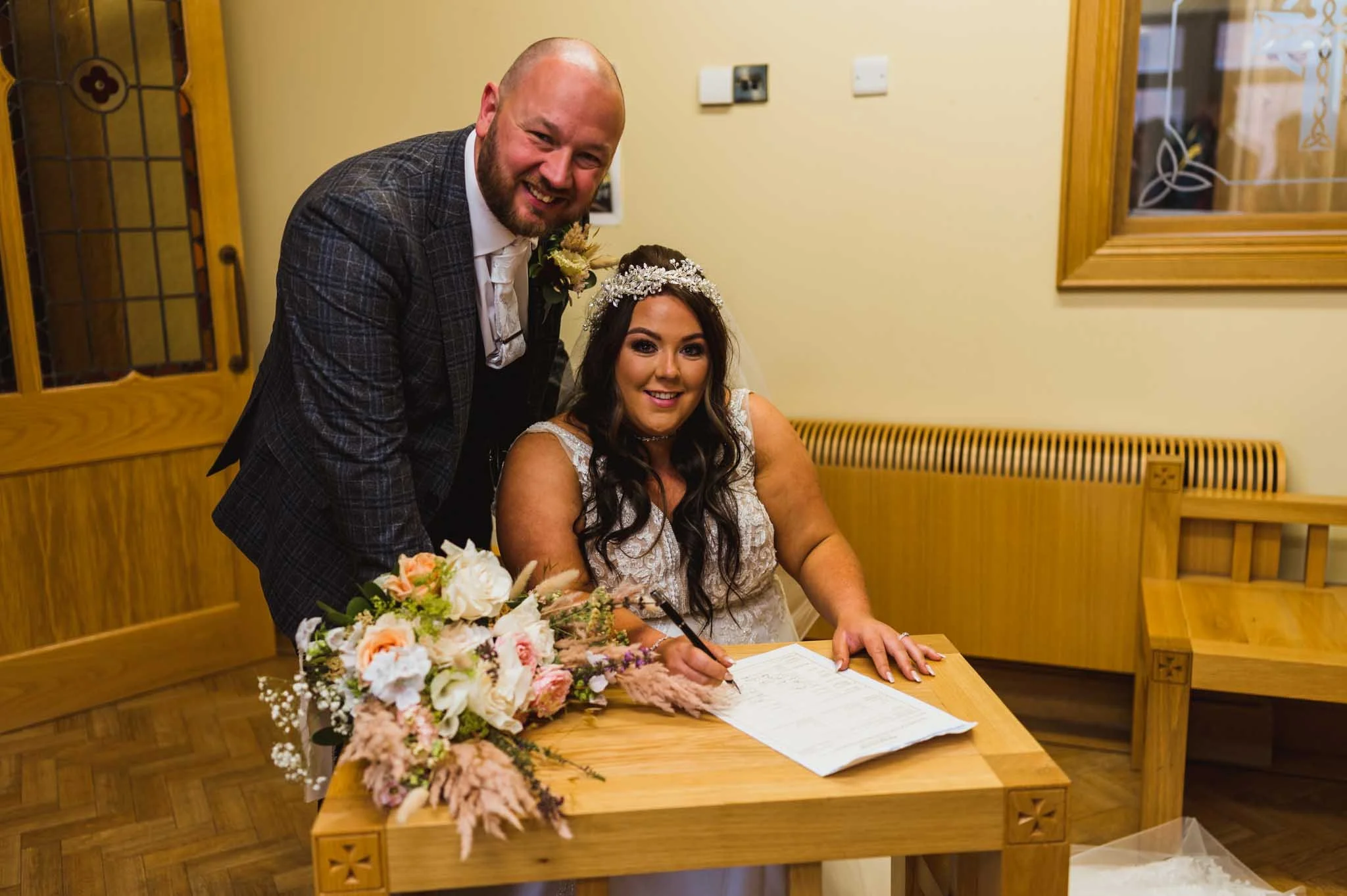 Photo of the new husband and wife signing the book, both looking smiling, looking at my camera.