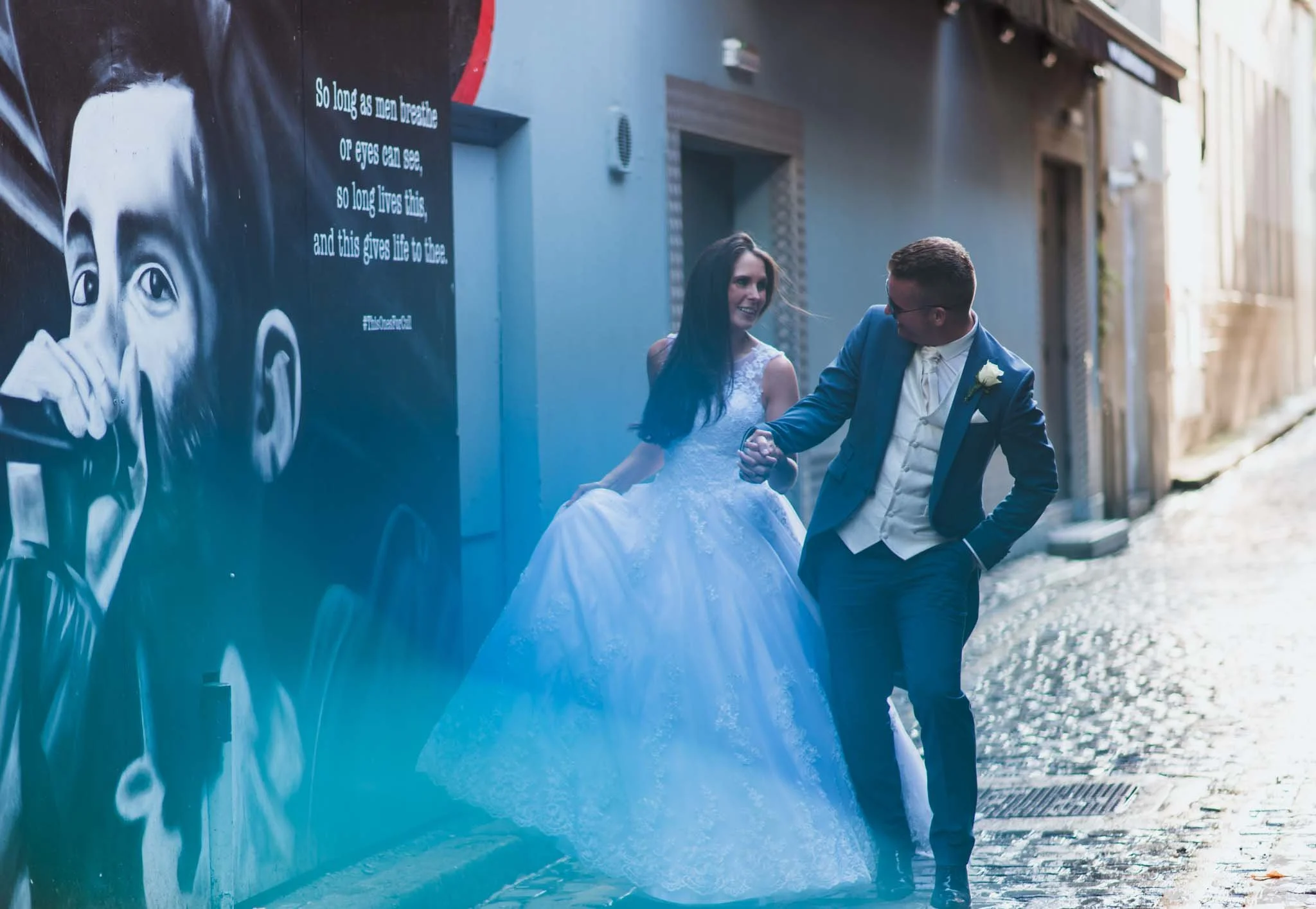 Bride and groom holding hands in an urban setting in a Belfast side street with a mural.