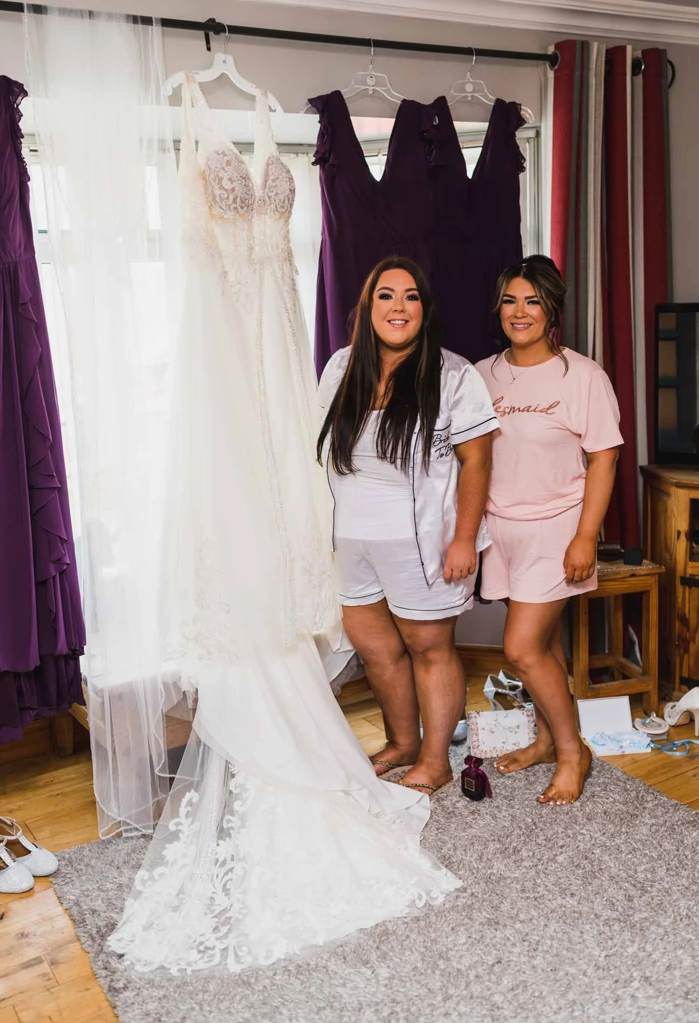 The bride with the maid of honour photographed beside the dress hanging up.