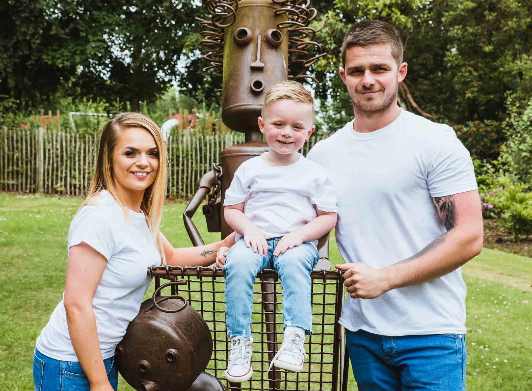 The two young parents with their son are sitting at a metal sculpture.