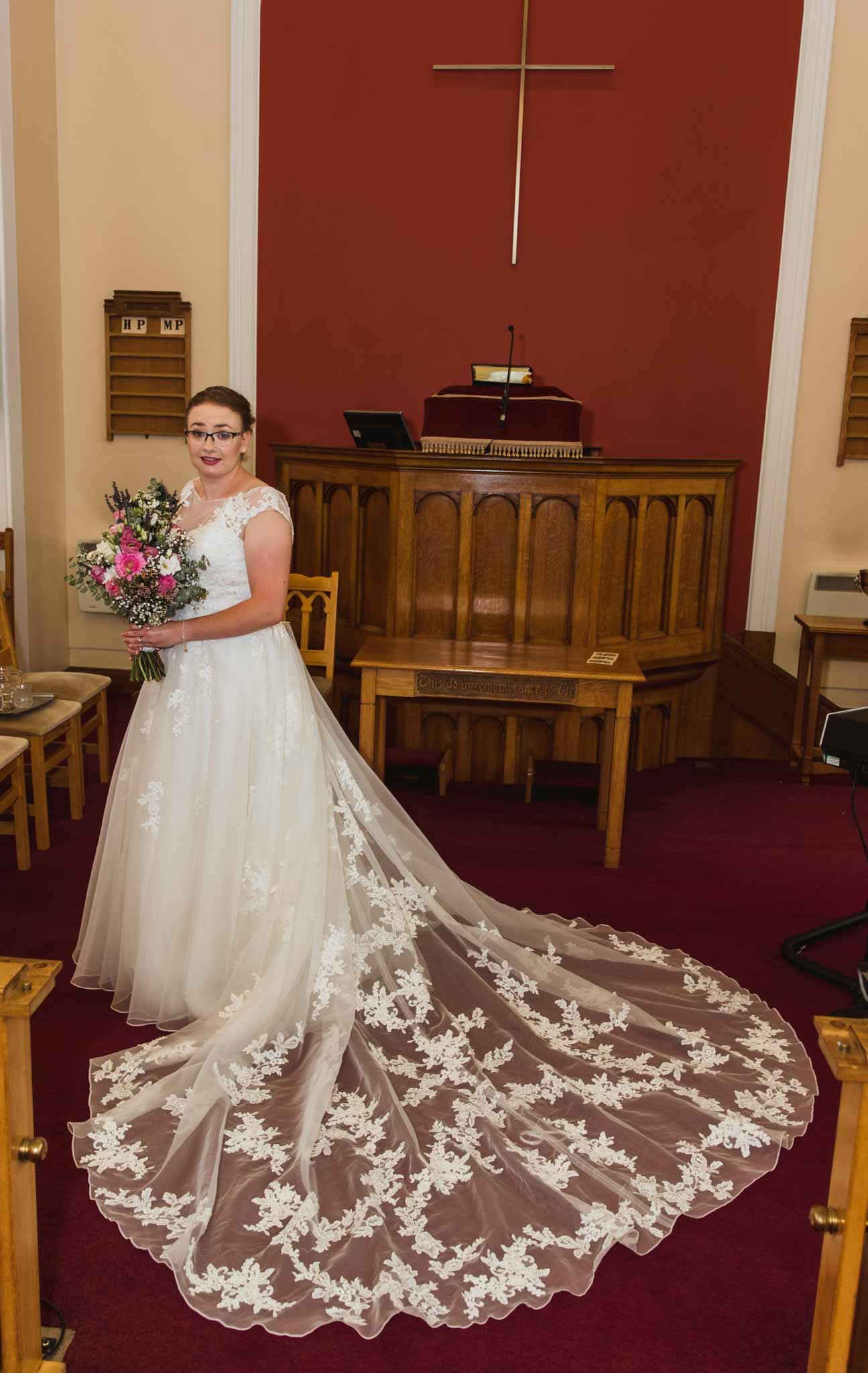 Portrait of the bride showing the back of her dress at the front of the church.