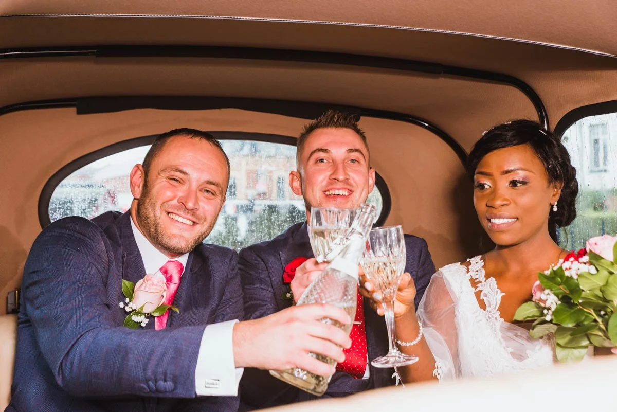 Bride, groom, with groomsmen holding champagne glasses in the limo.