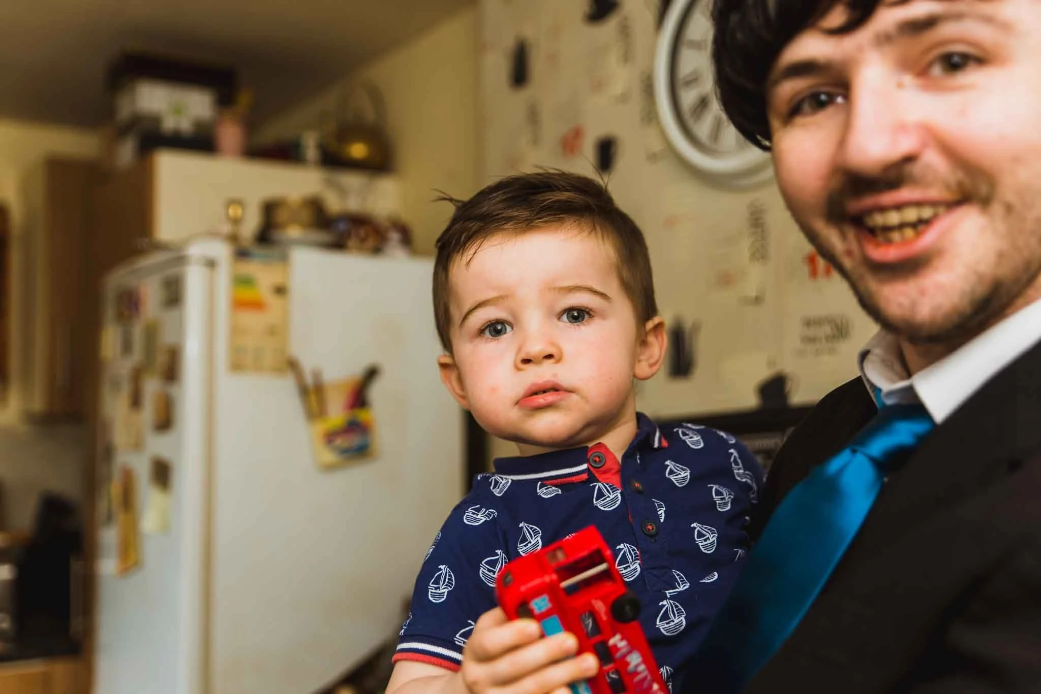 The bestman holding a baby in the kitchen.