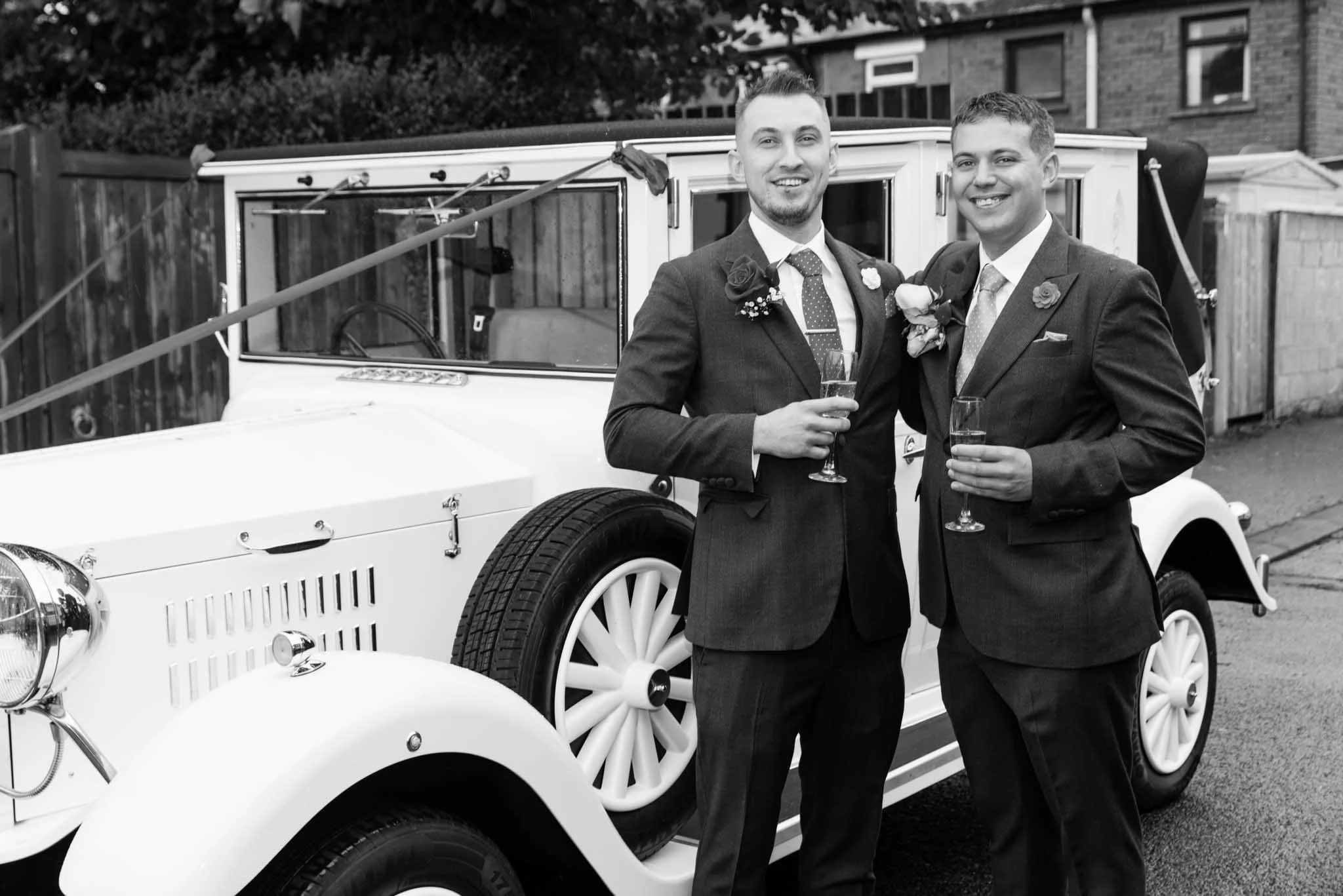 Mono image of the groom and bestman with champagne beside their limo.