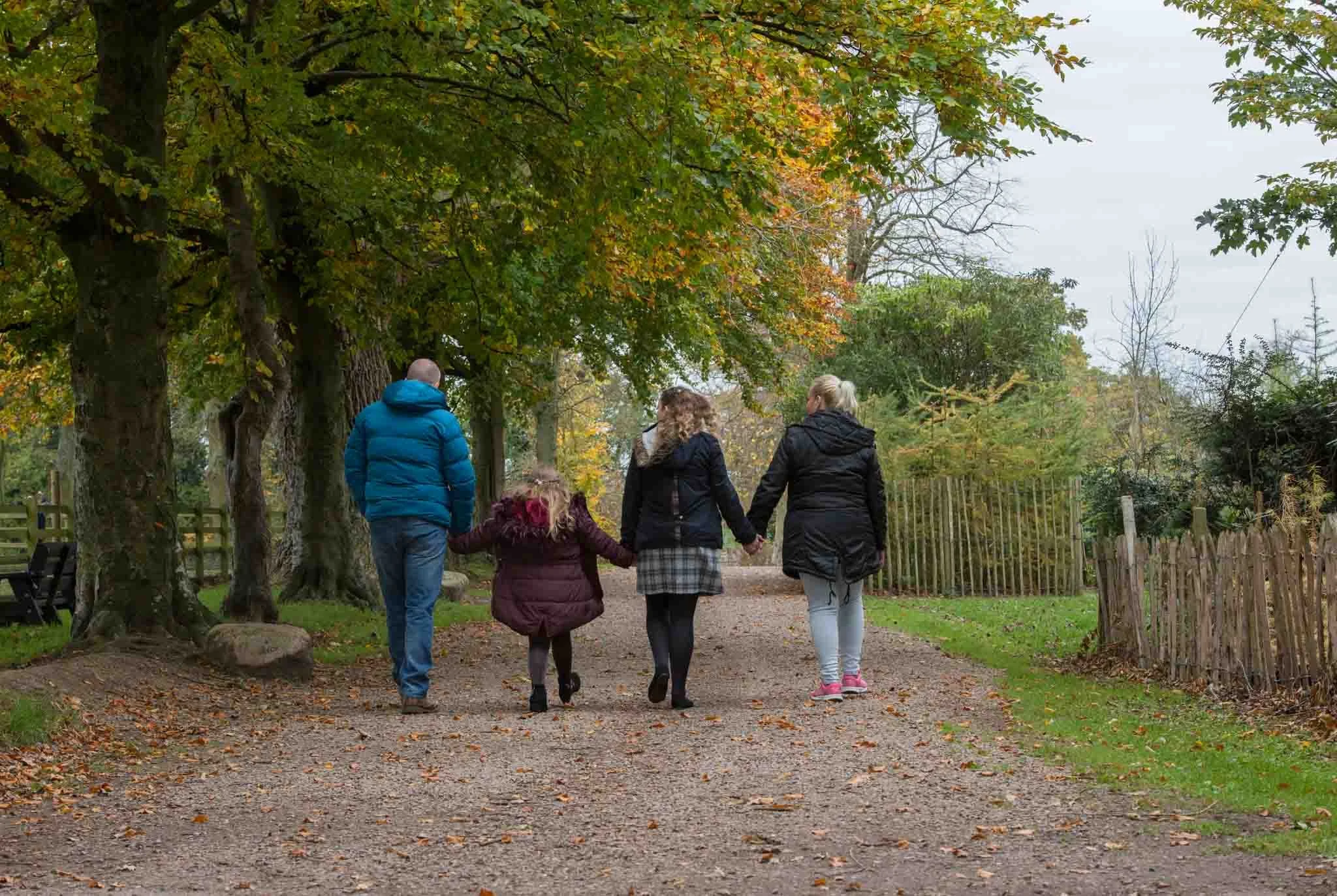 Photographed from the back as the family hold hands walking along the path.