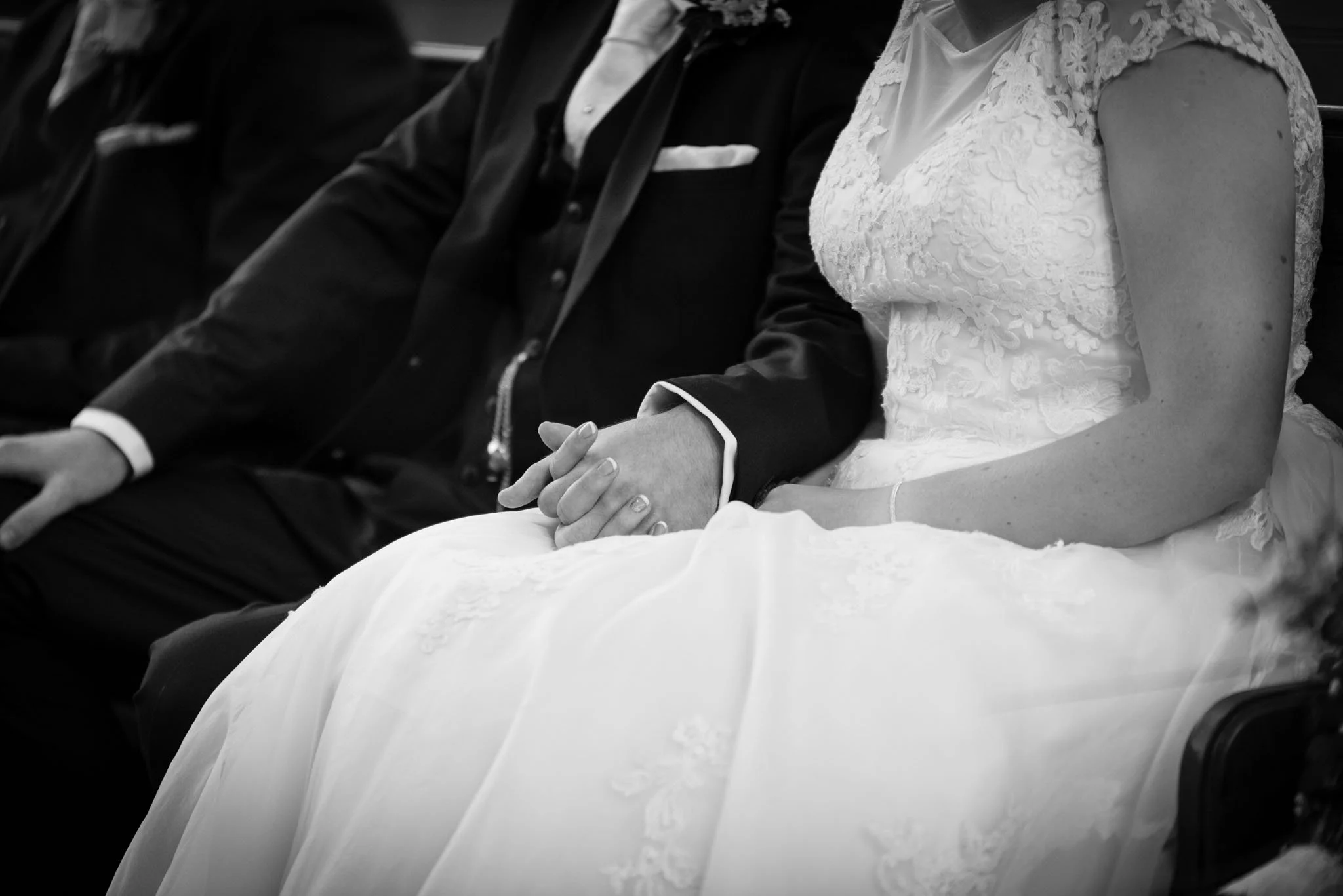 Close-up of bride and groom holding hands, black and white.