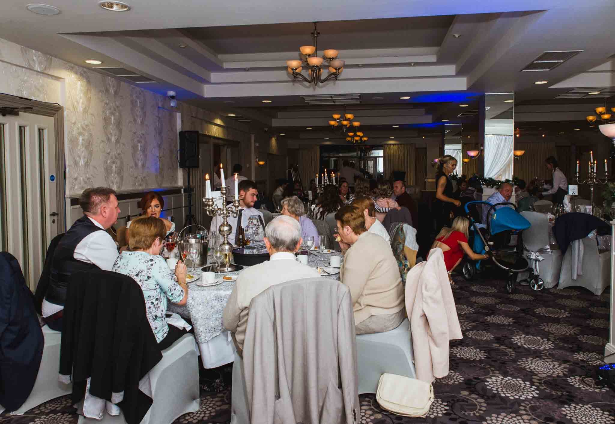 Guests are sitting at tables with a waiter serving food.