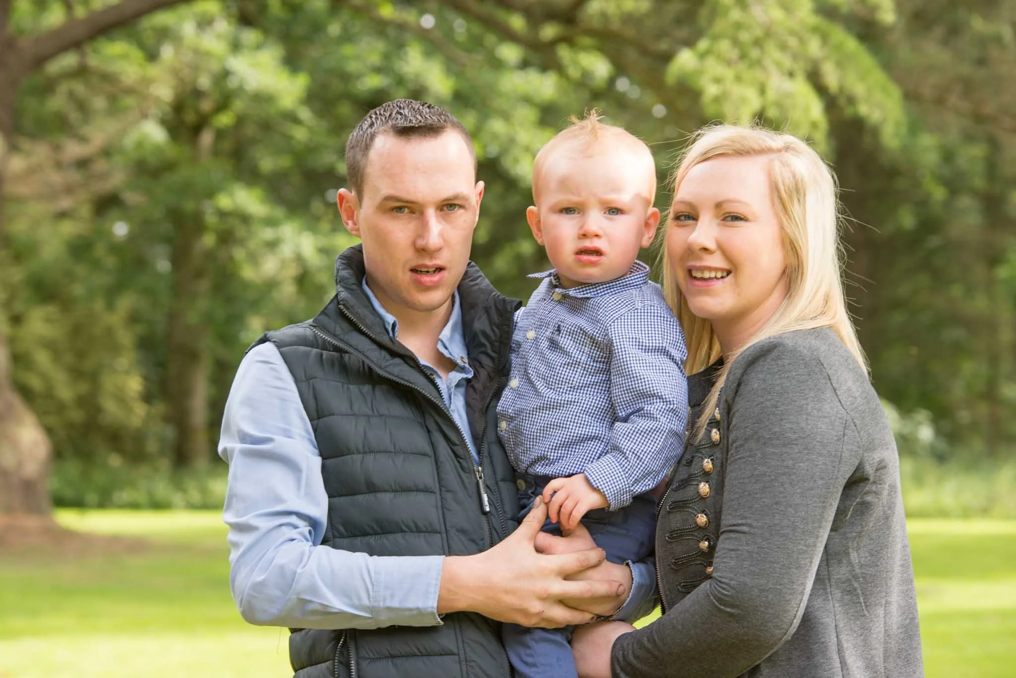 Dad holding son with mum beside them smiling in the forest.