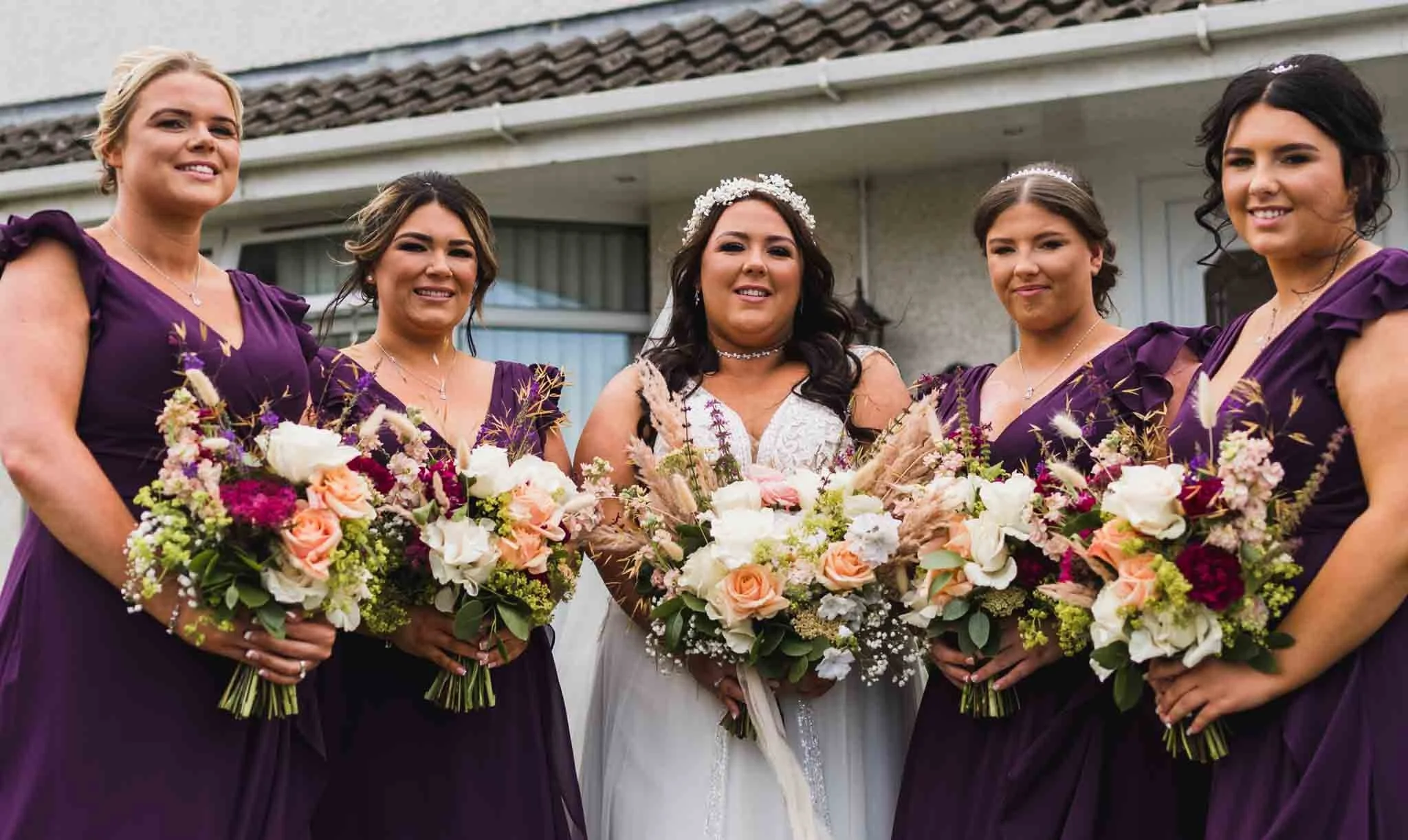 Bridal party in a semi-circle with bouquets, looking at my camera.