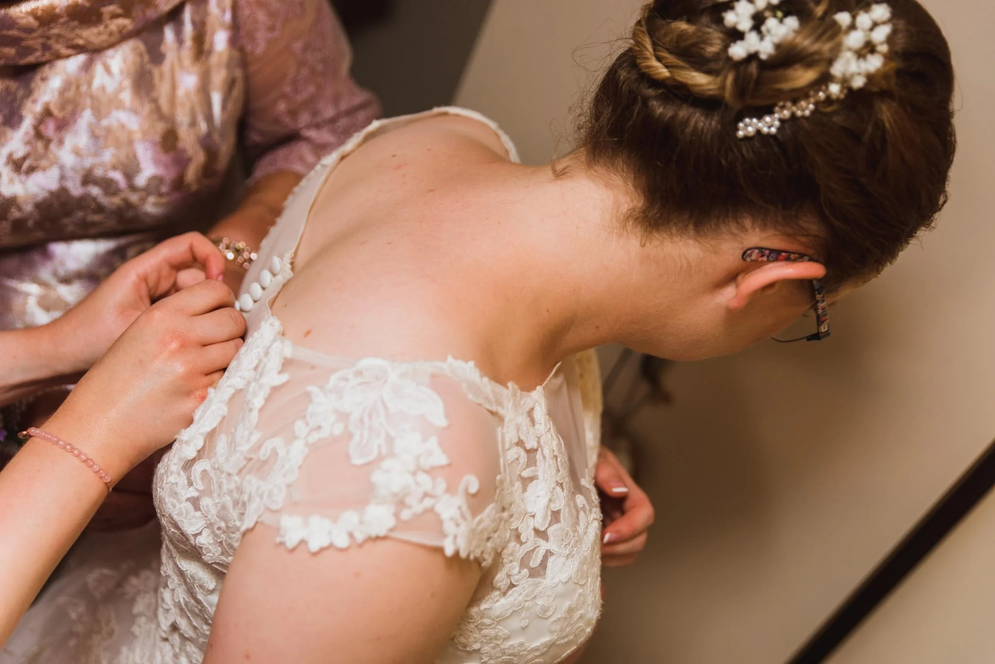 Bridesmaids helping put the bride's dress on from the back.