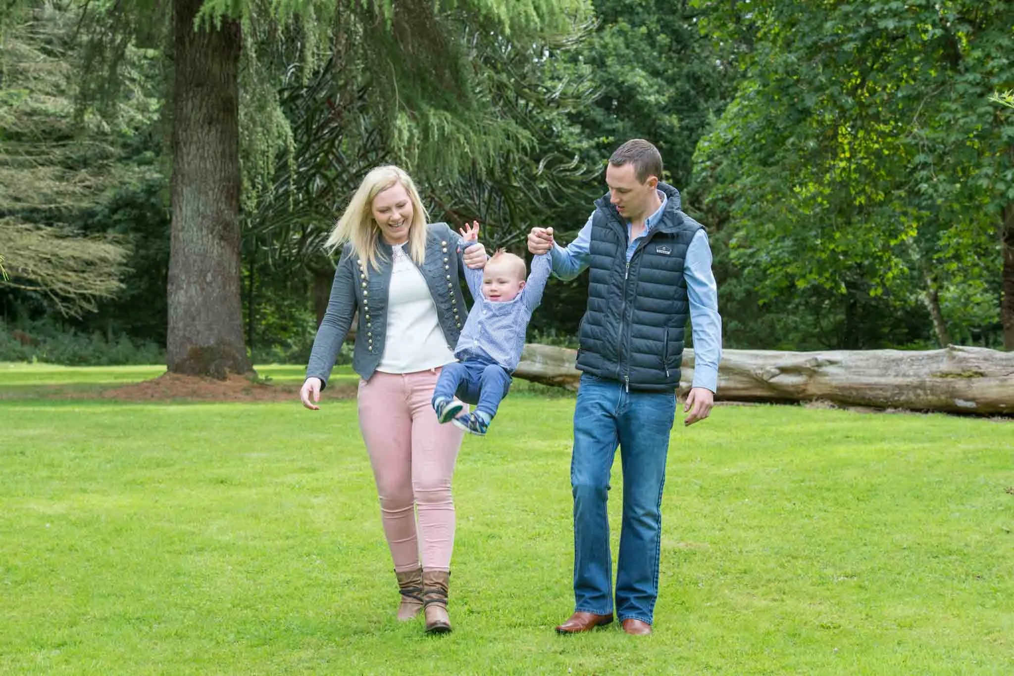 Mum and dad swing their young child for fun in the park.