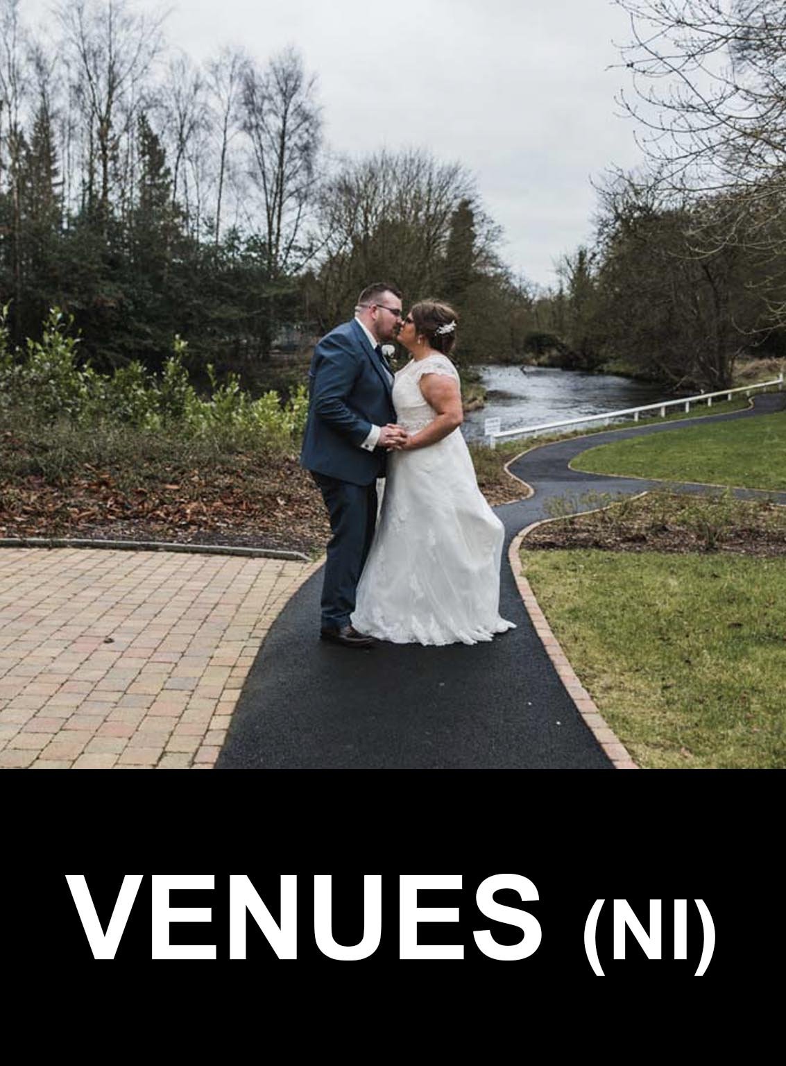 The bride and groom kiss on the path in front of the river.