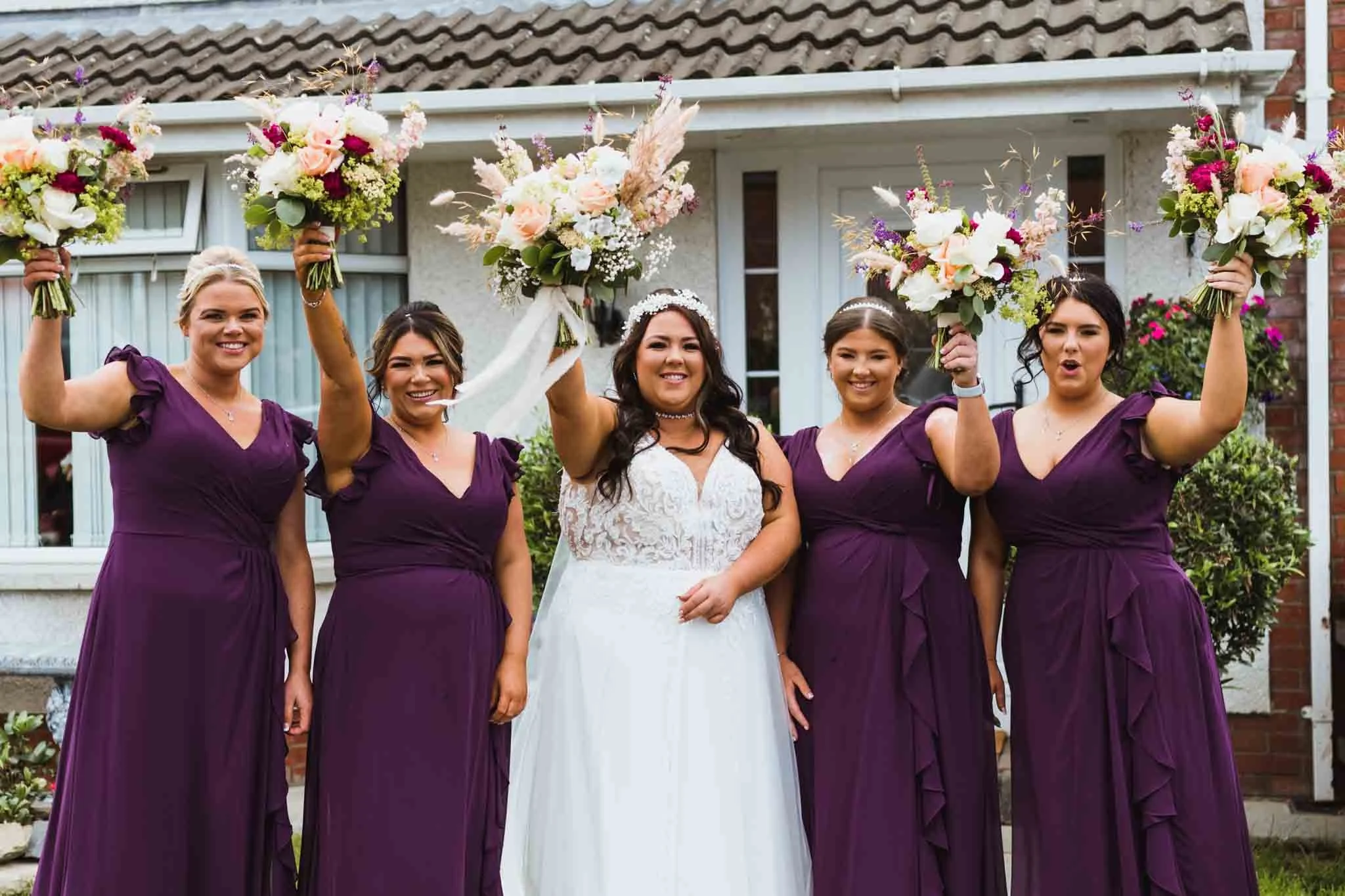 Bride with bridal party cheers, holding bouquet up.