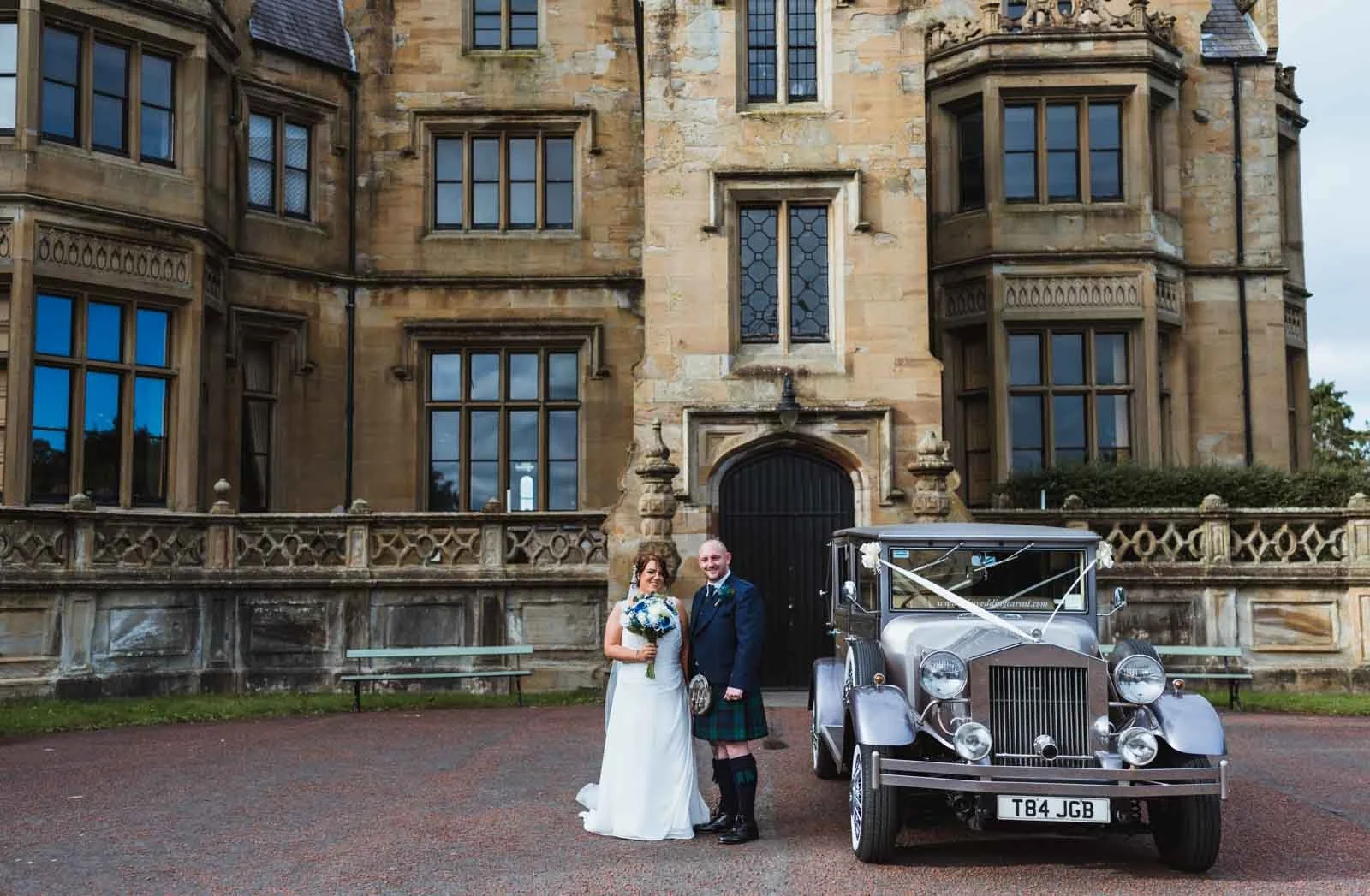 Bride with bouquet and groom beside limo at the front of Brownlow House.