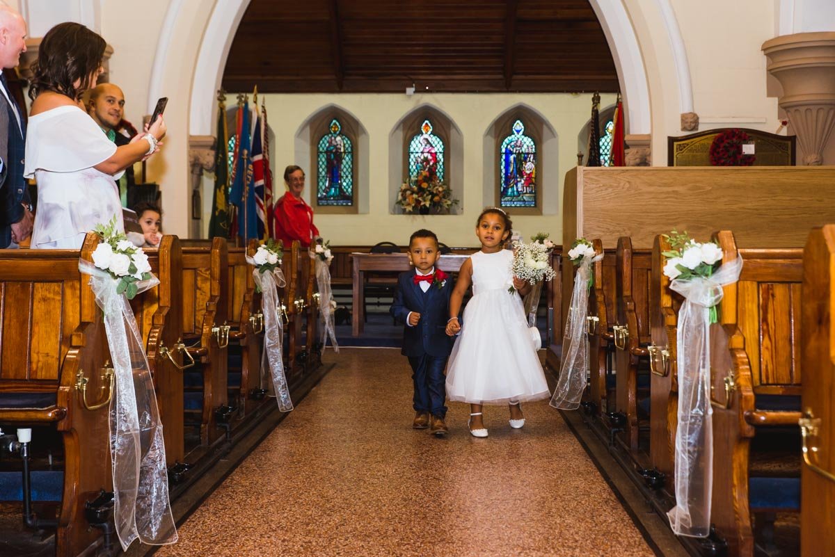 A coloured boy and girl walk down the aisle in the church.
