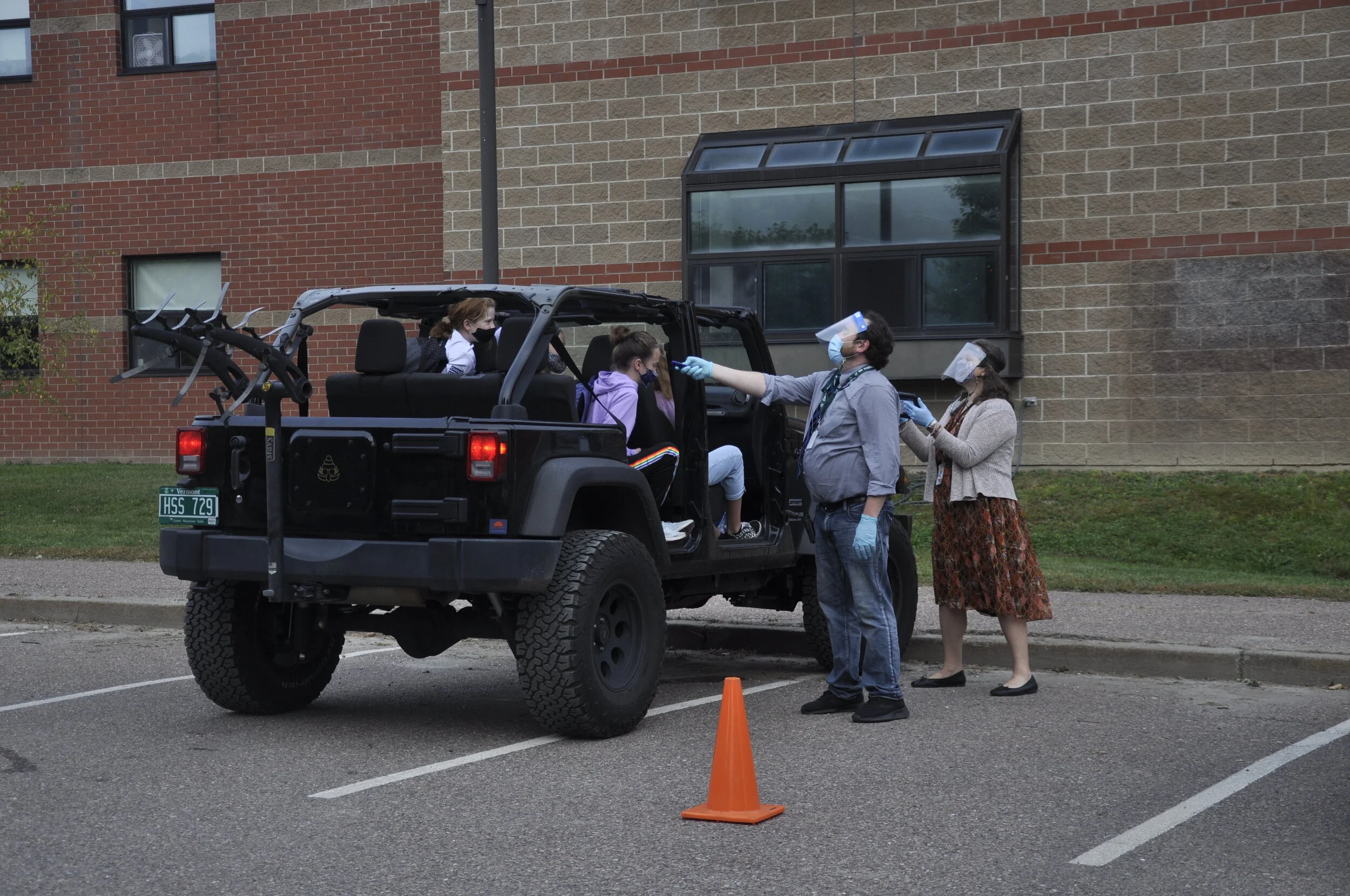  Assistant Principal Josh Estes does the temp checks and School Counselor Jen Hempey asks the health questions before students hop out. Photo by Lisa Scagliotti.  