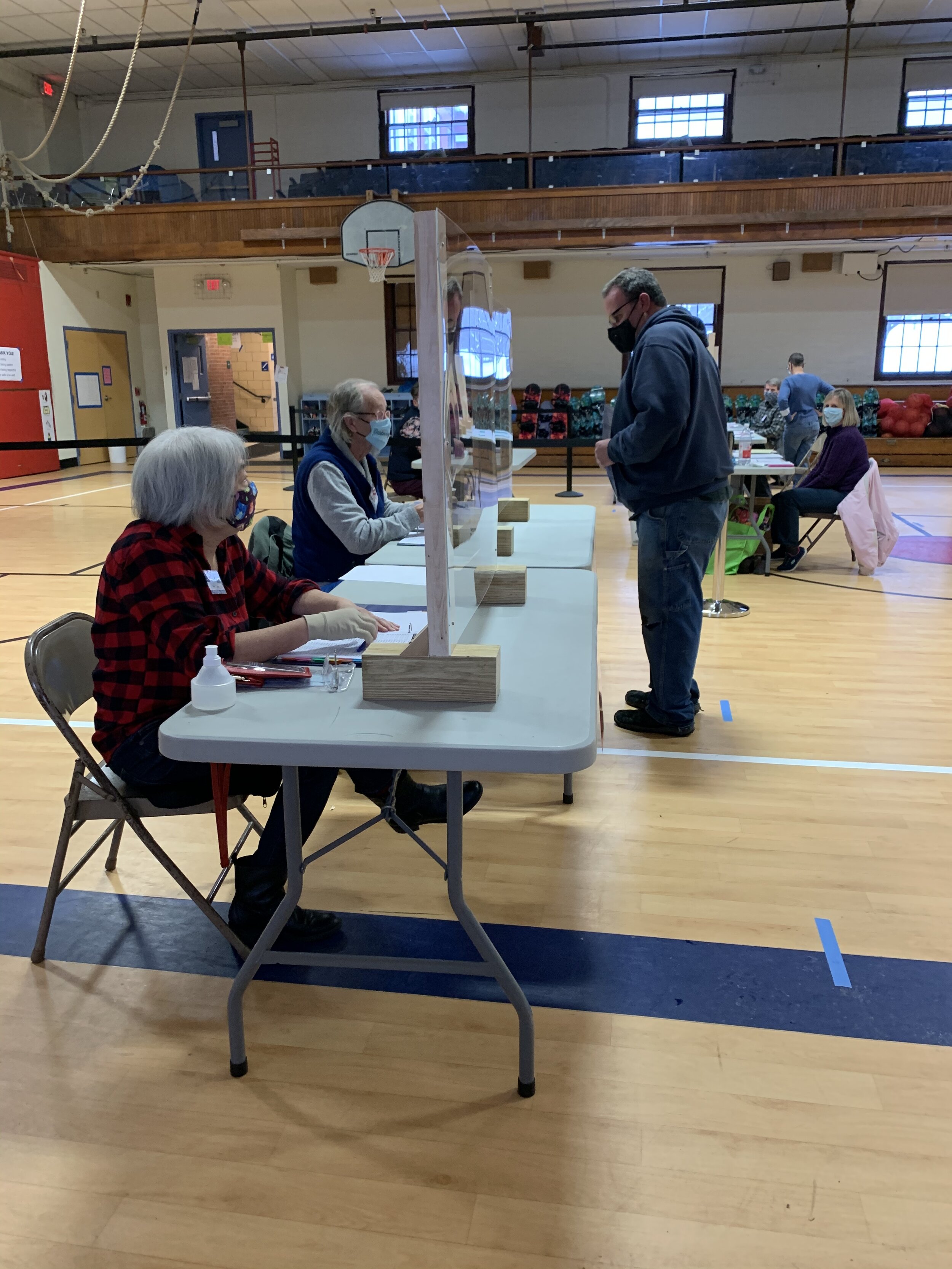   Election volunteers Pauline Nolte and John Bauer sit behind Plexiglas shields at their checking stations inside Thatcher Brook gym on Tuesday. Photo by Lisa Scagliotti.  