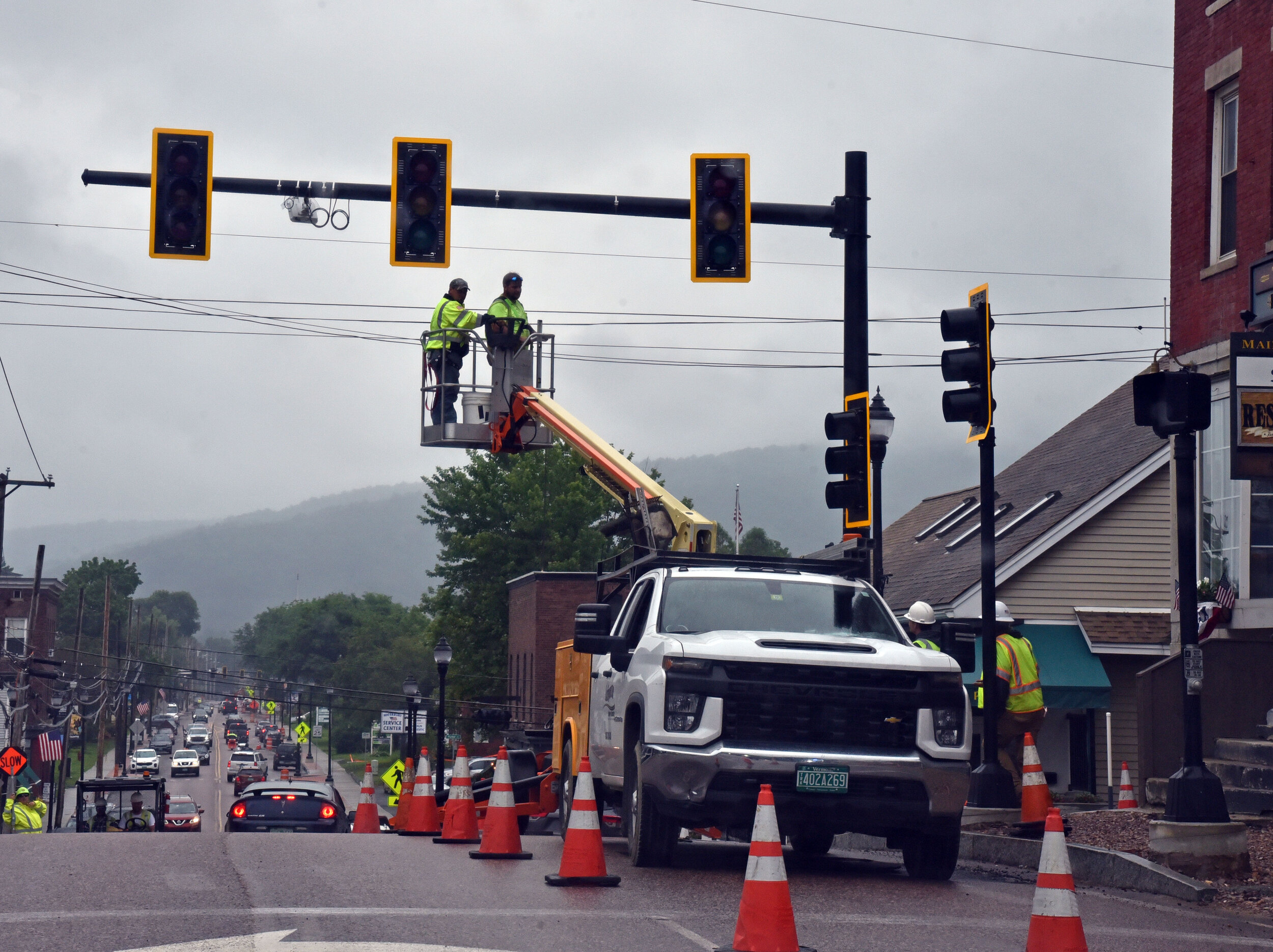   Traffic moves along and around workers making final adjustments to the traffic signals at the Main and Winooski Street intersection. Photo by Gordon Miller  