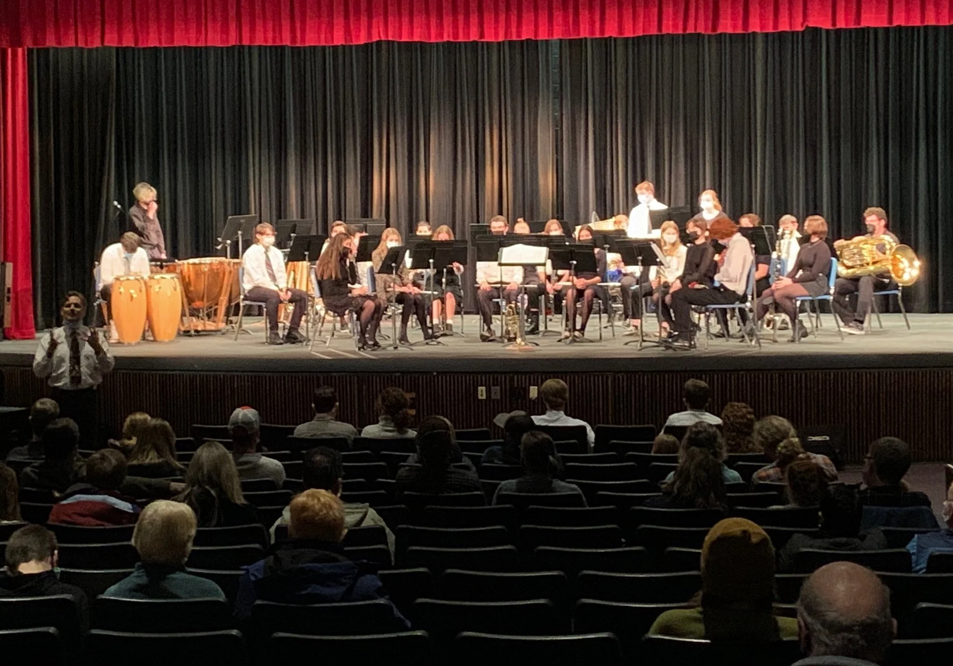  Masked audience members are seated in family groups with space for distancing as Band Director Chris Rivers (far left) opens the performance with remarks. Photo by Lisa Scagliotti  