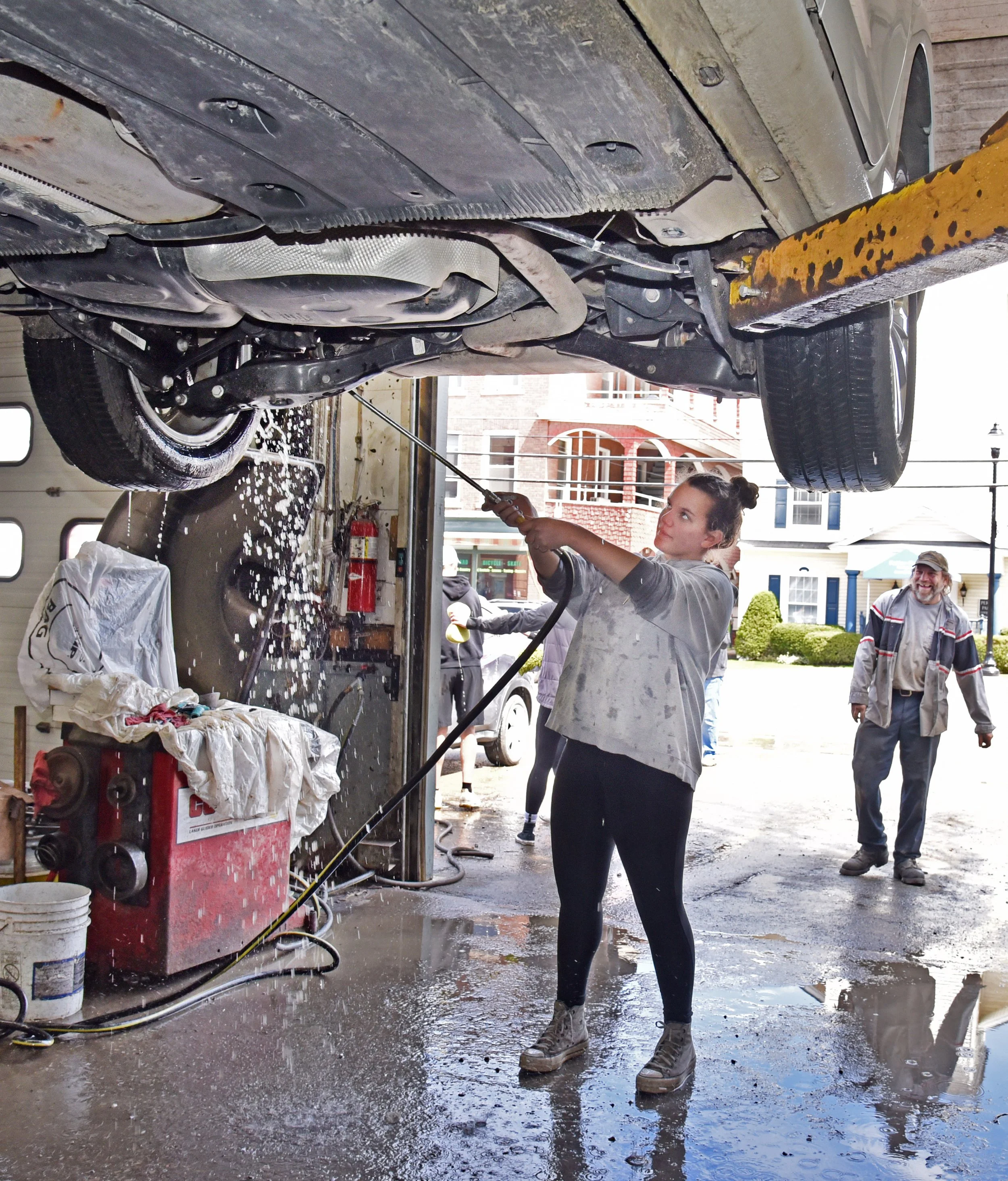   Abby Young, a member of the Harwood Girls Basketball team, washes the undercarriage of a car last Saturday at Waterbury Service Center while station owner Albert Caron looks on. Photo by Gordon Miller  