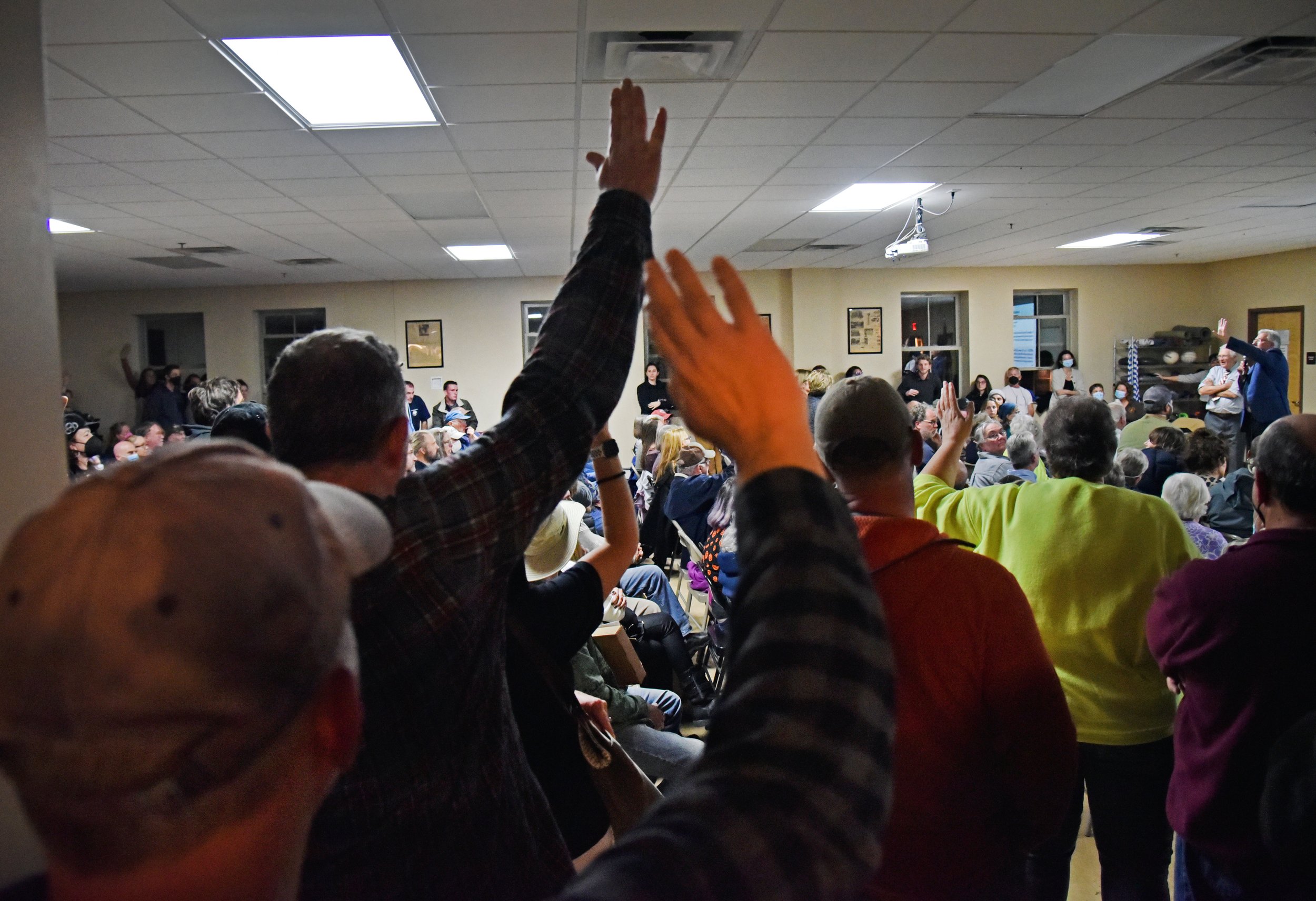  People raise their hands to vote for using paper ballots. Photo by Gordon Miller  